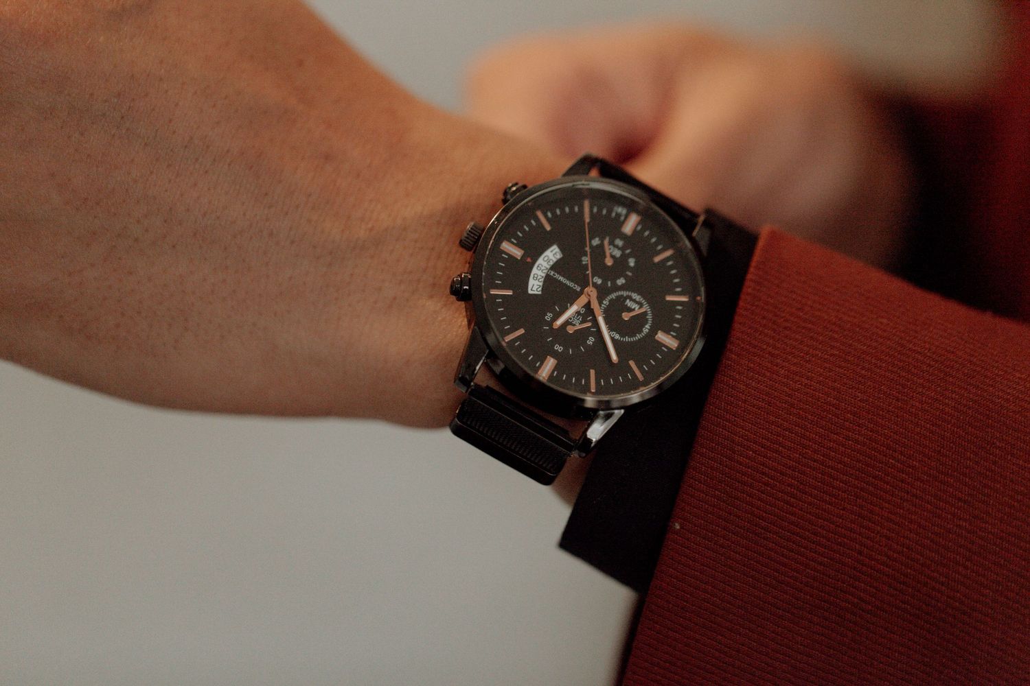 Black chronograph watch with leather strap being adjusted on wrist against dark background.