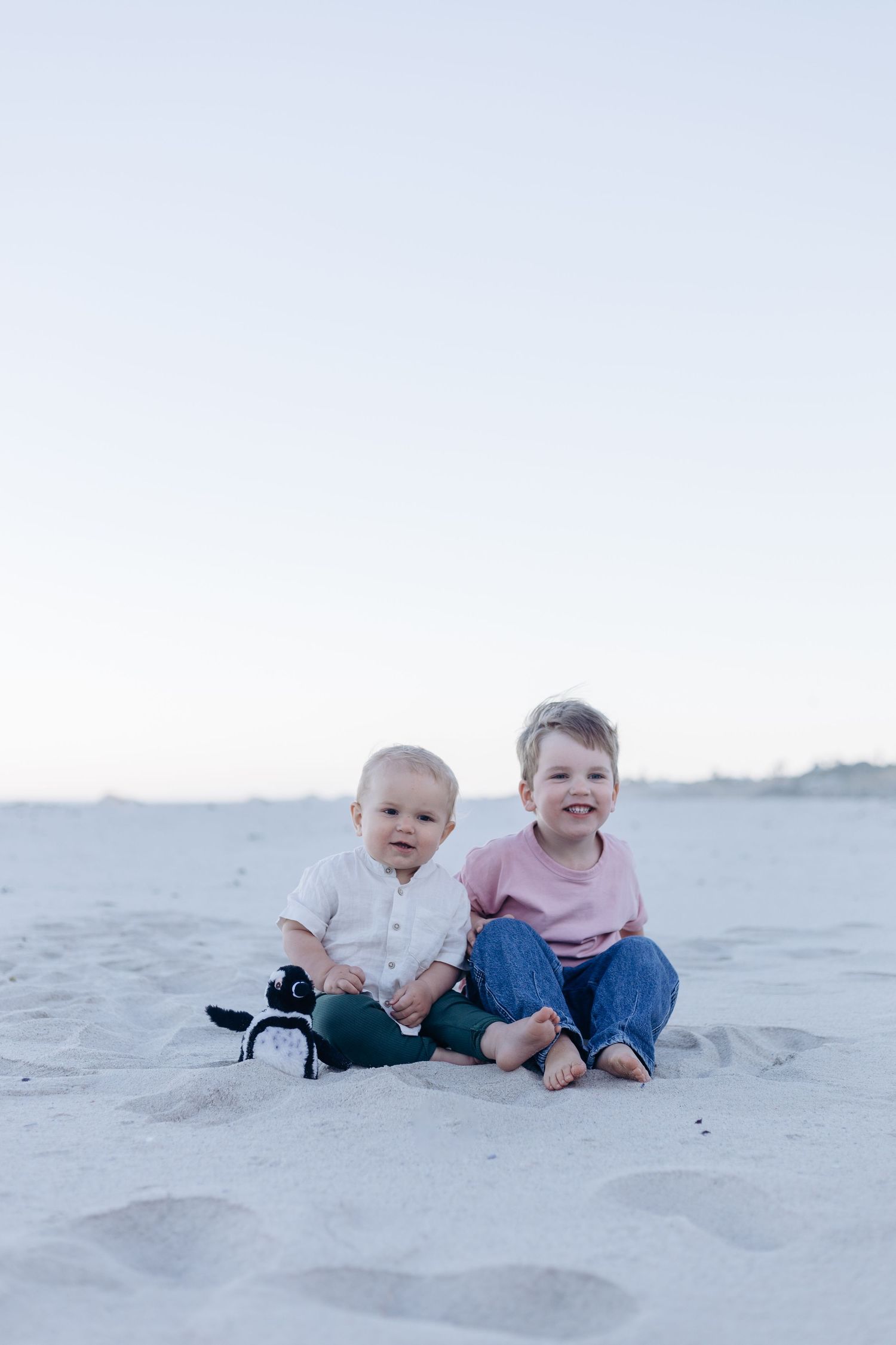 Two small children laying together and playing on pristine white sand at the beach during a bright sunny day.