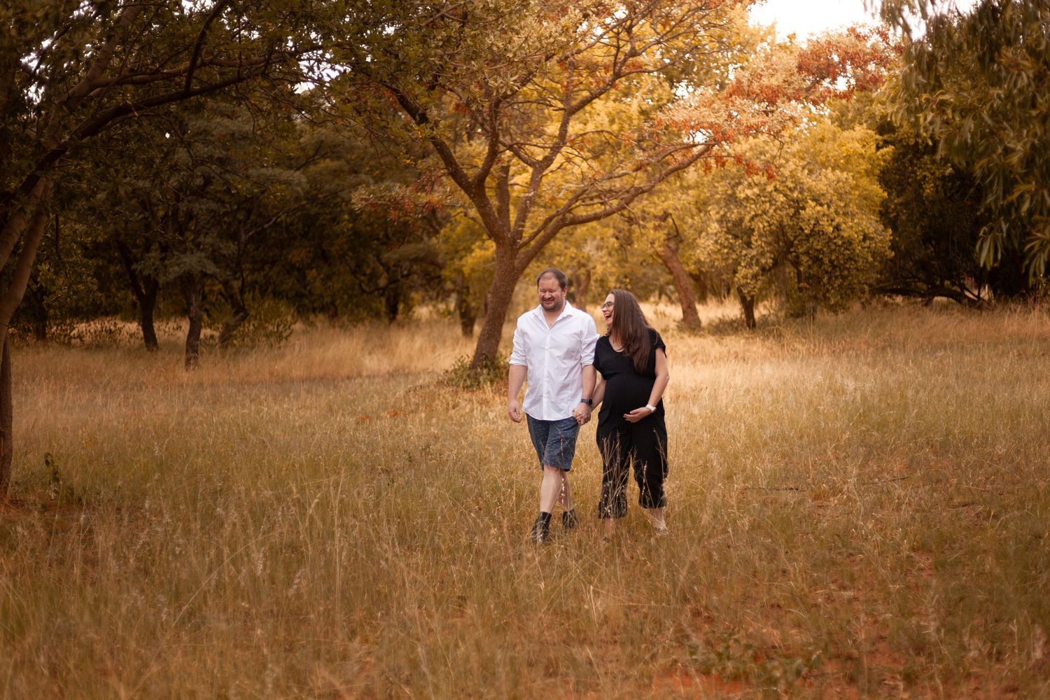 Family walks together through a golden autumn field at sunset creating silhouettes against the warm sky.