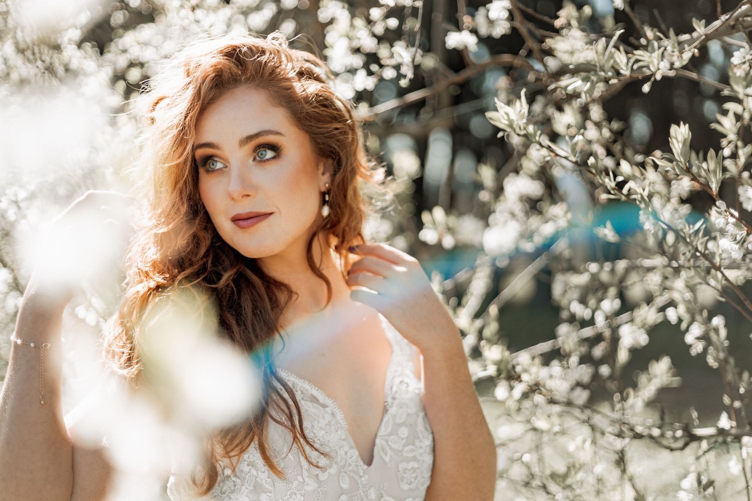A person with red hair poses among delicate white spring blossoms during a dreamy golden hour photoshoot.