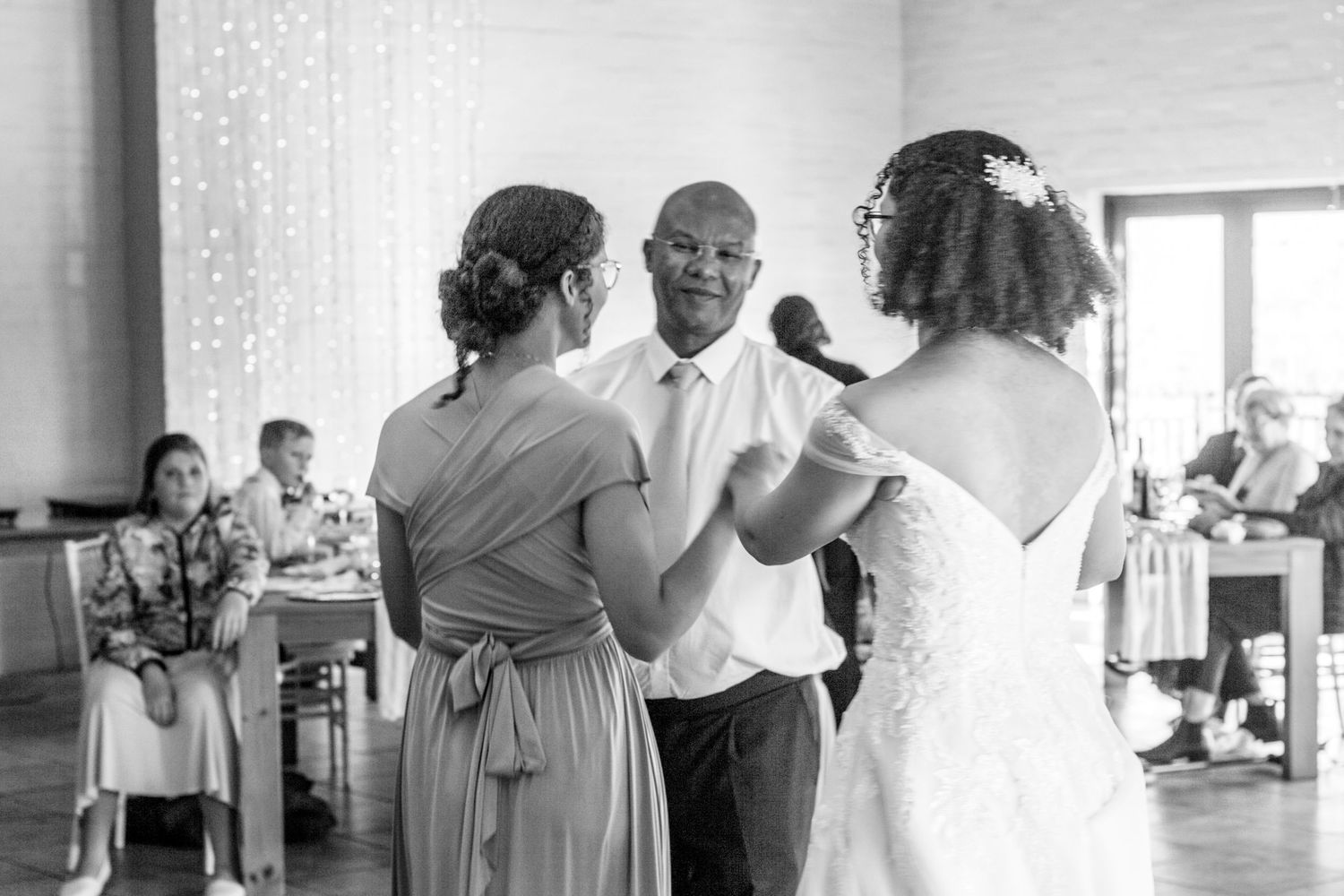 Black and white images of guests dancing together and embracing during a wedding celebration at an indoor venue.