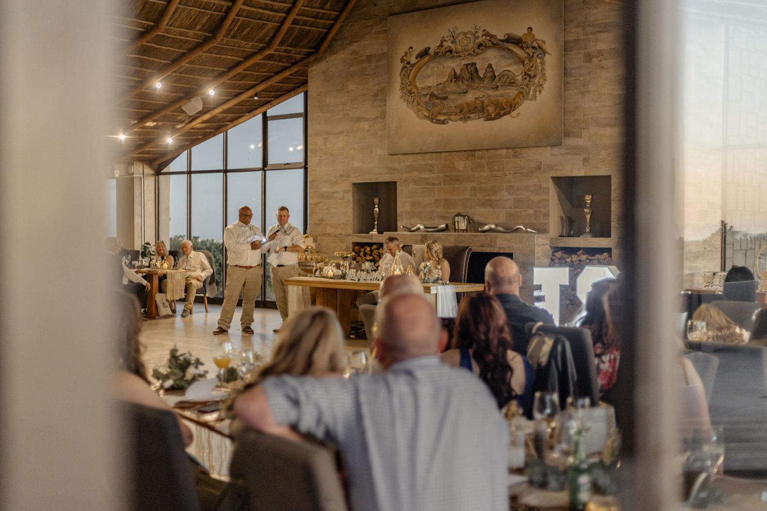 Wedding guests enjoy a reception in an elegant ballroom with warm lighting and rustic wooden beams.