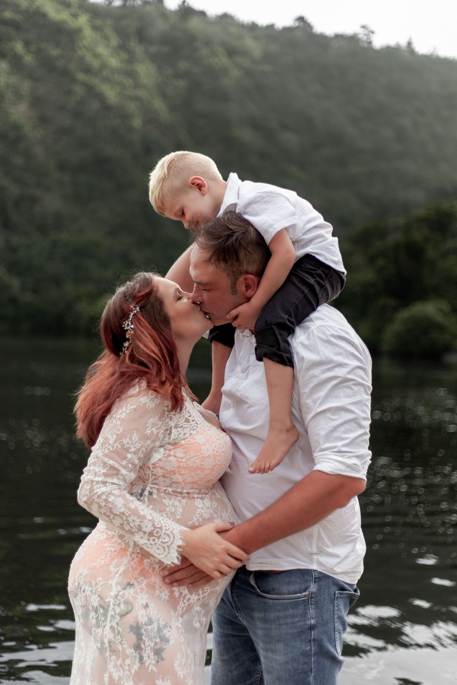 A romantic maternity photo session at a lake shows an expecting couple in coordinating outfits sharing tender moments.