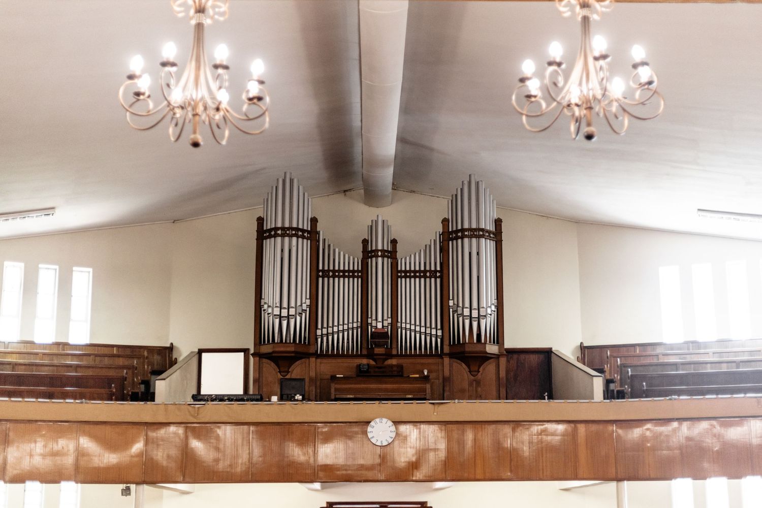A large wooden pipe organ with brass pipes sits above wooden pews in a traditional church sanctuary.