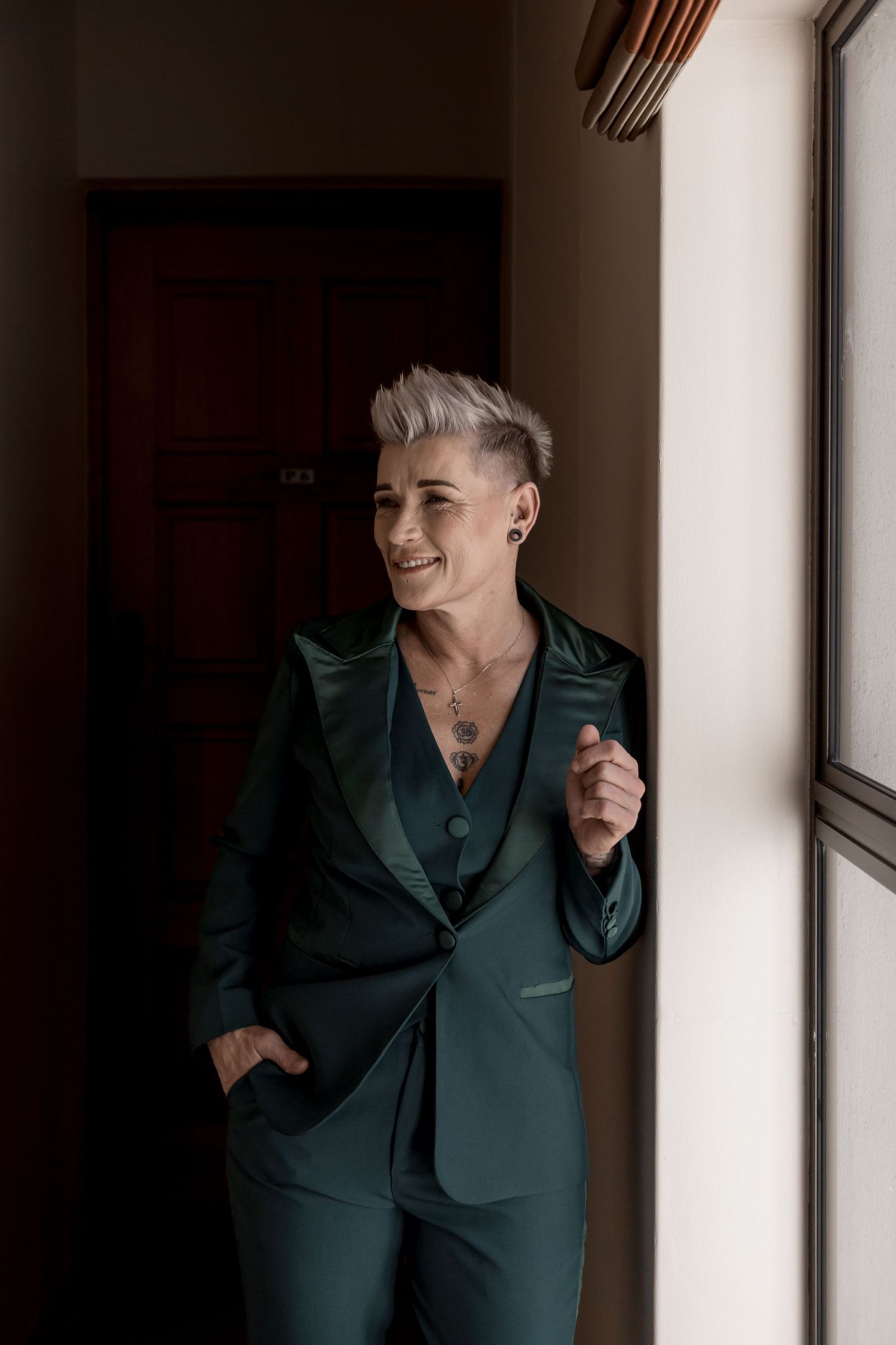 A person in a dark green suit poses playfully in a series of four connected photos against a white wall.