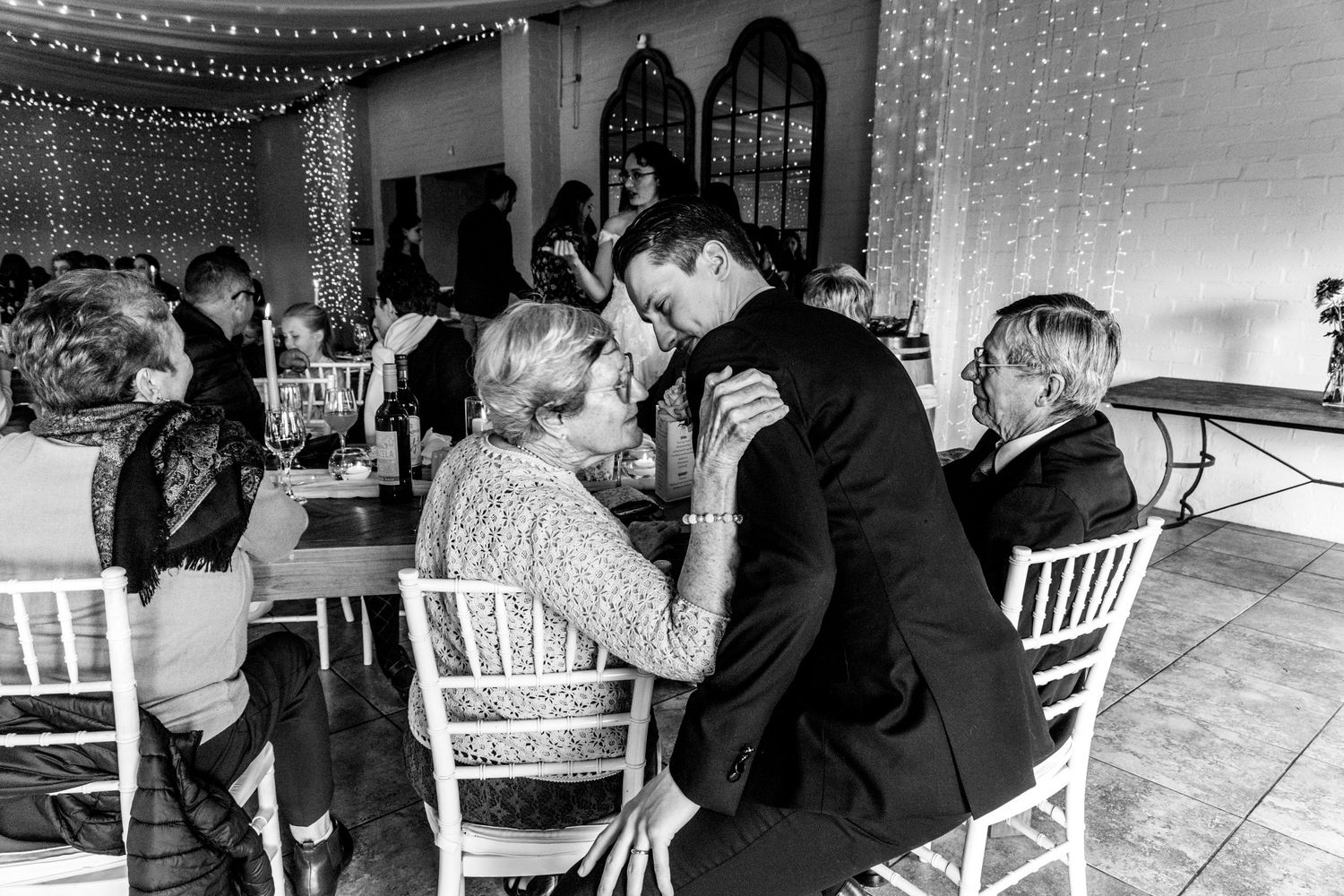 A panoramic wedding reception sequence showing tables and chairs with fairy light decorations in black and white.