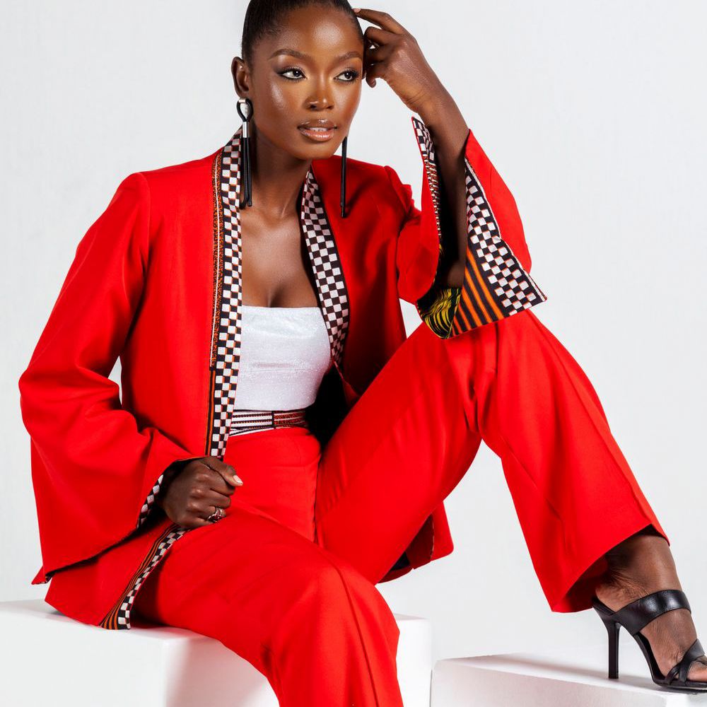 Model wearing red pantsuit with checkered trim poses elegantly on white backdrop.