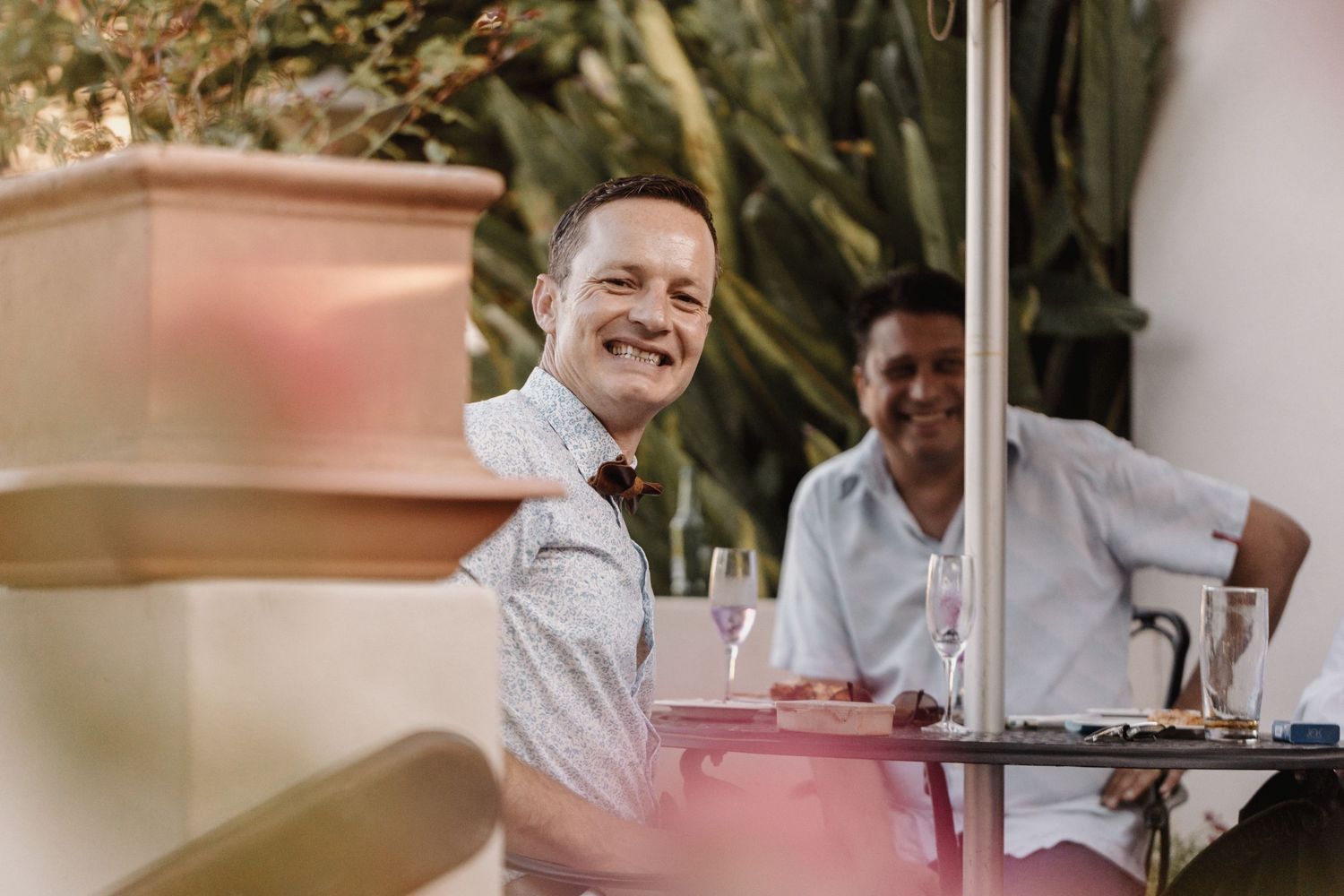 Group of professionals discuss and laugh during a sunny outdoor meeting on a restaurant terrace.