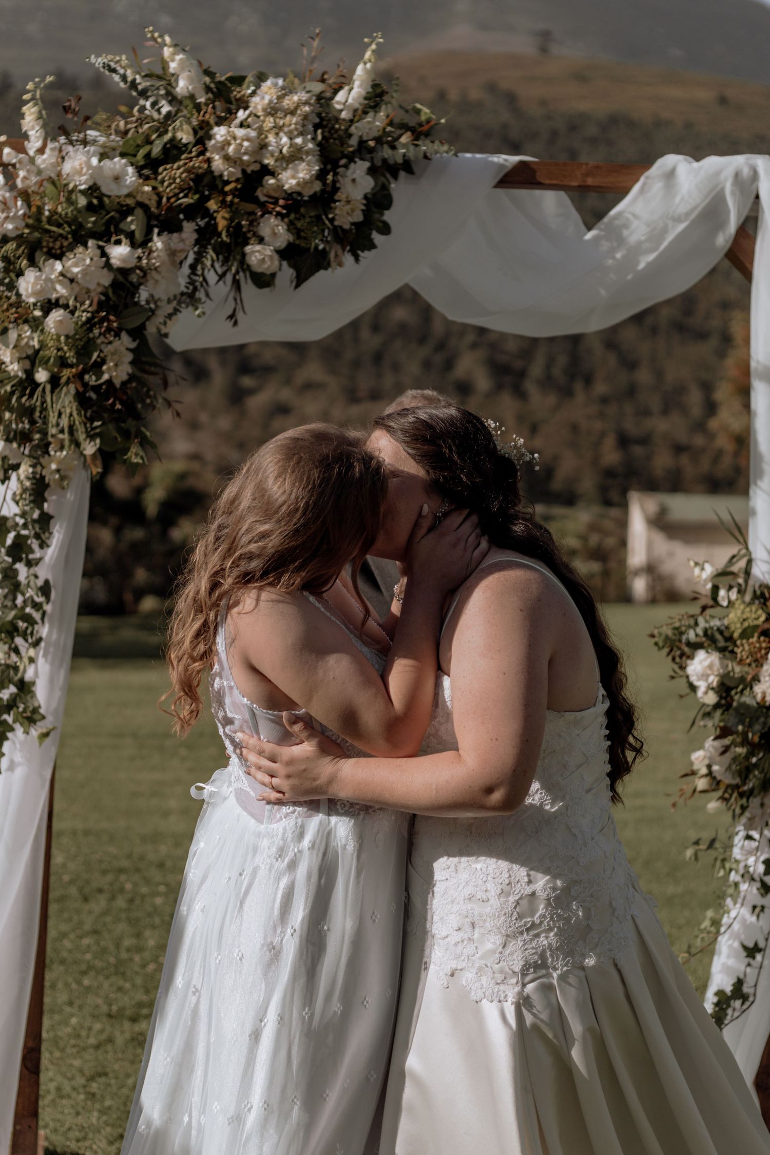 Wedding ceremony moment with white floral arch and matching lace dresses against a scenic mountain backdrop.