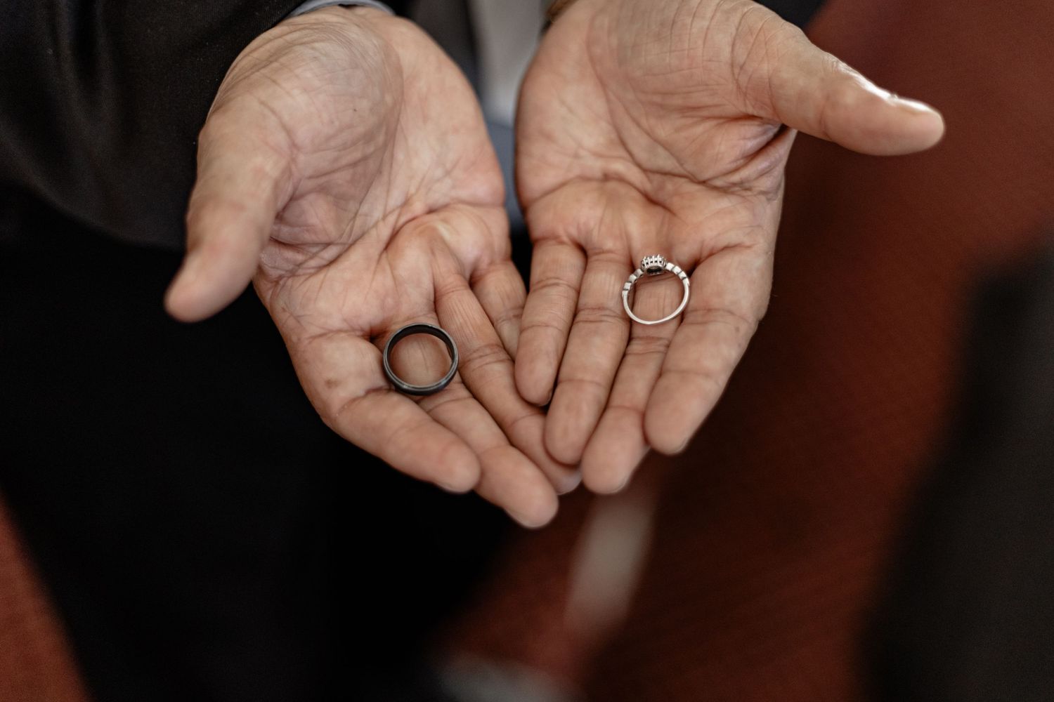 Close-up shot of hands holding wedding rings on a dark background with warm lighting.