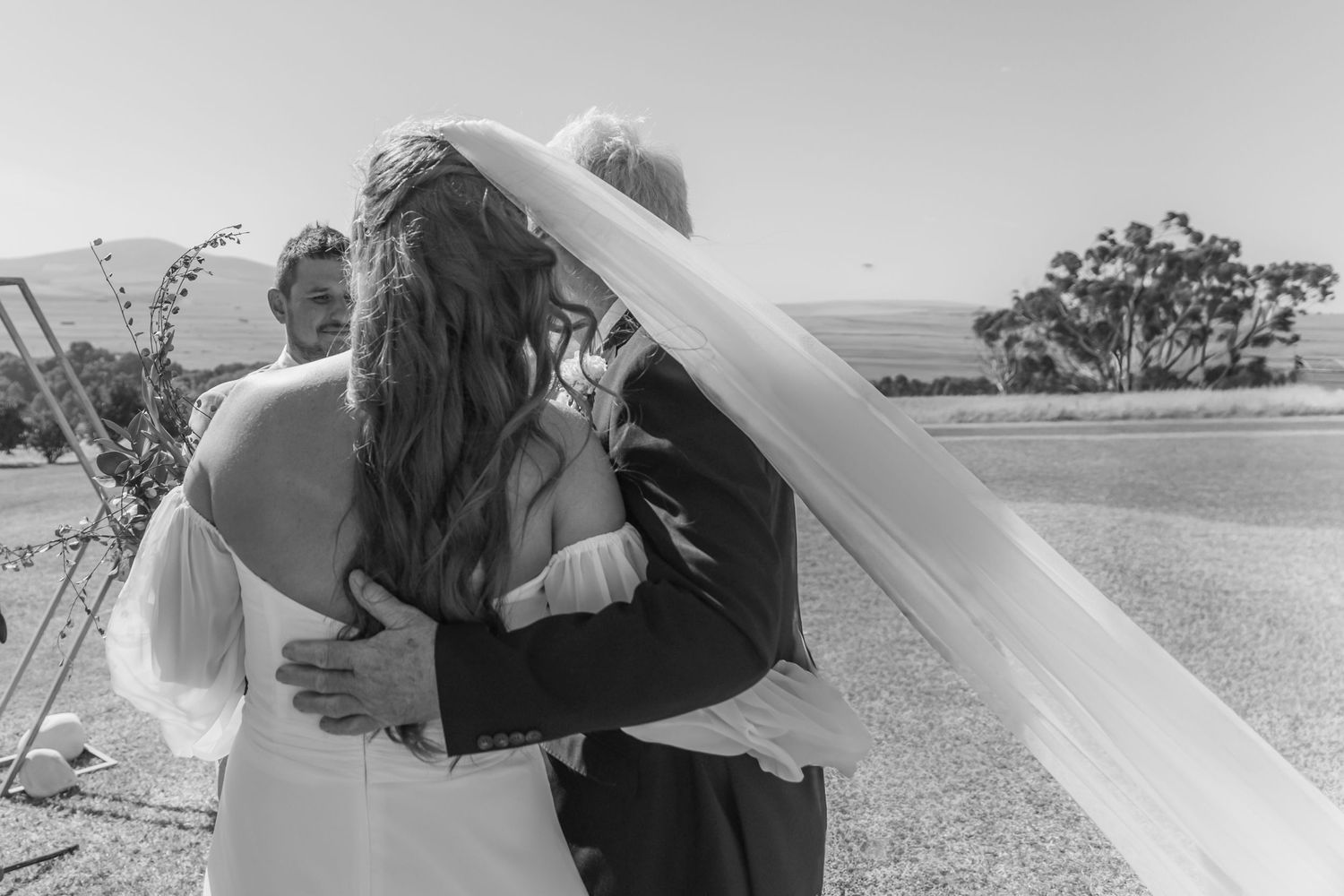 Black and white photo of a bride and groom sharing a heartfelt embrace during their outdoor wedding ceremony.