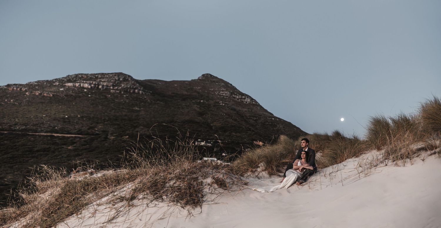 A panoramic sequence of sandy beach dunes with mountain peaks in the background during golden hour lighting.