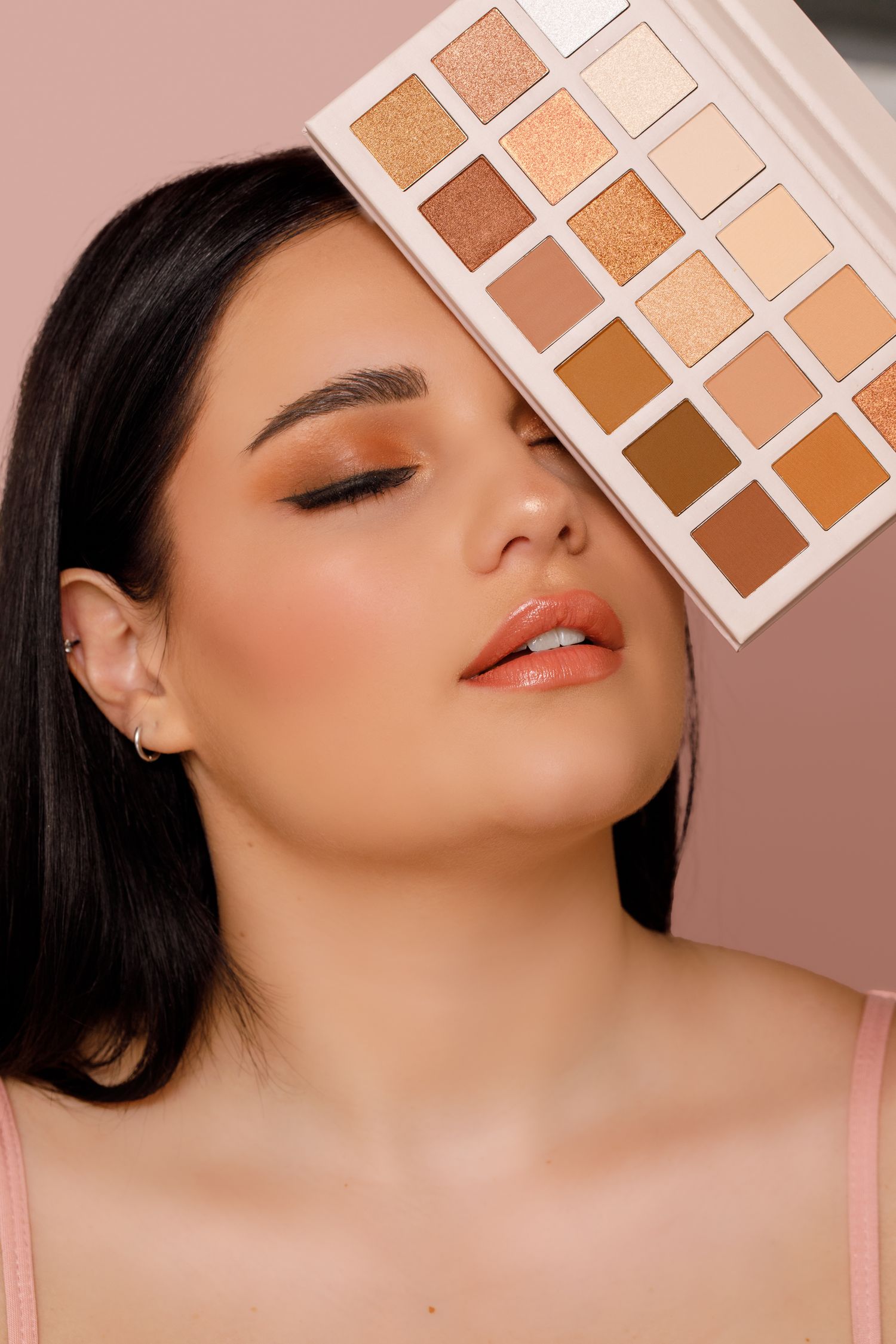 Makeup palette with warm neutral eyeshadow shades shown next to model wearing peachy bronze eye look and coral lips.
