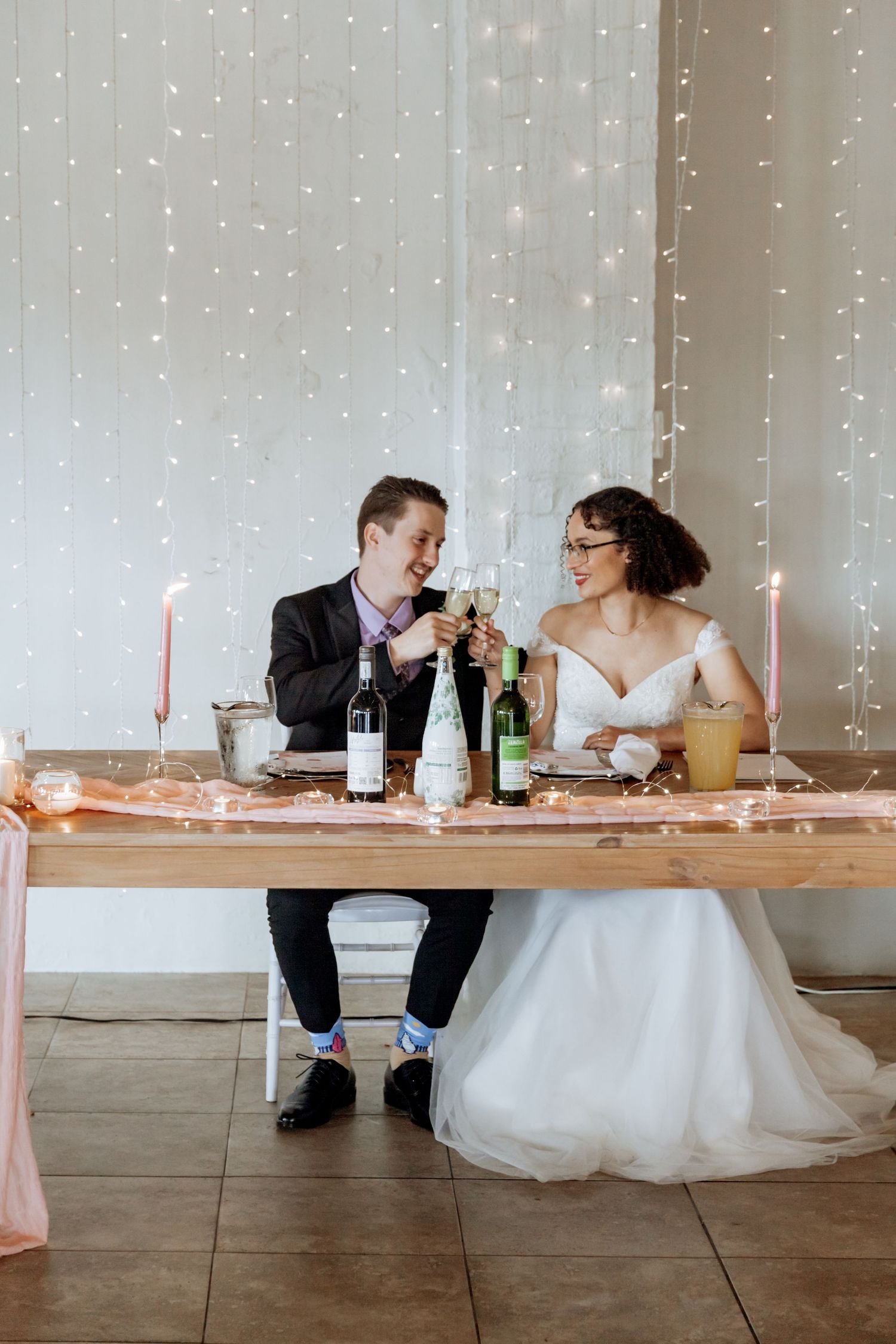 A bride and groom share an intimate moment at their wedding reception table with string lights glowing in the background.