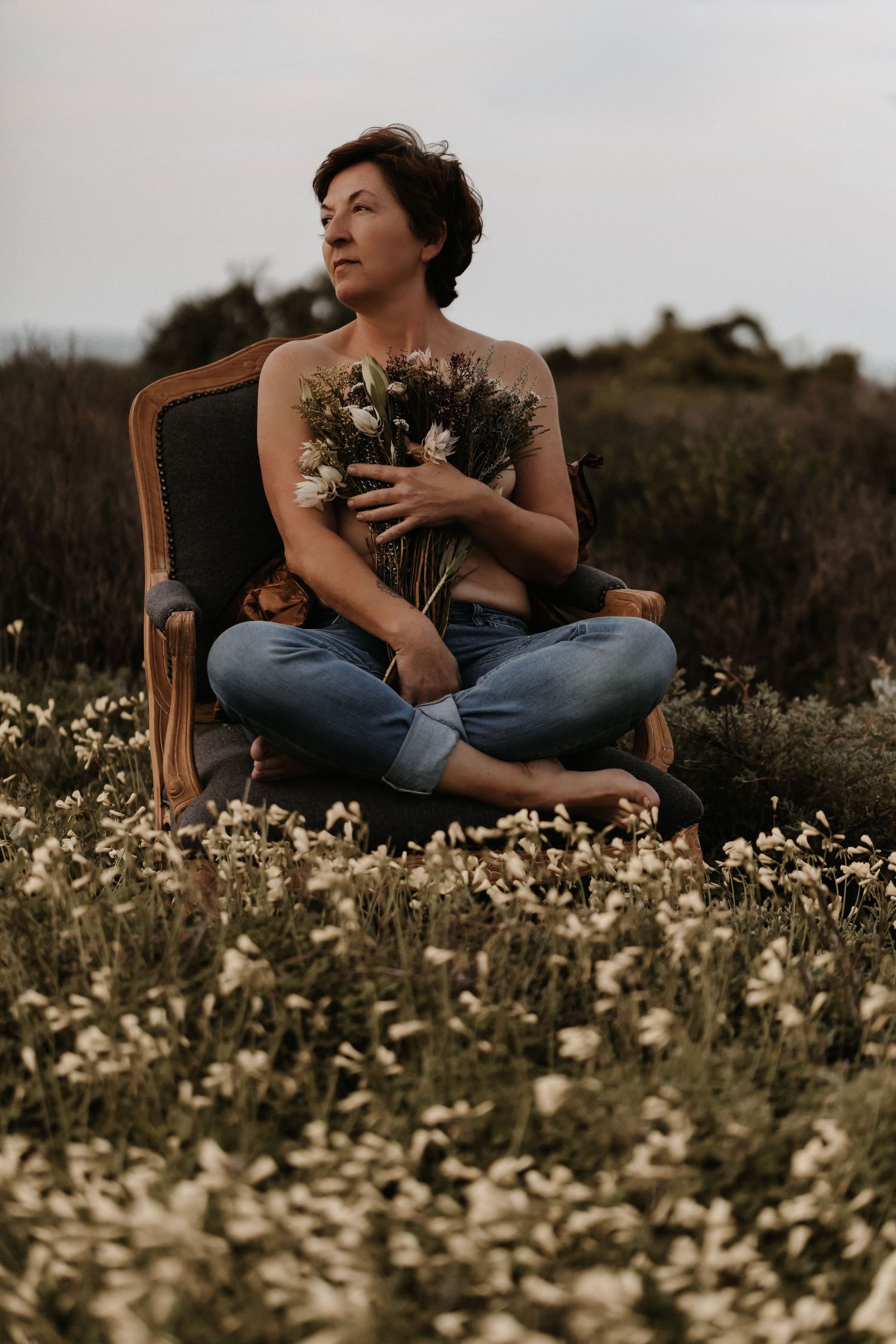 A person sits in a wooden chair amidst a field of blooming white wildflowers during golden hour.
