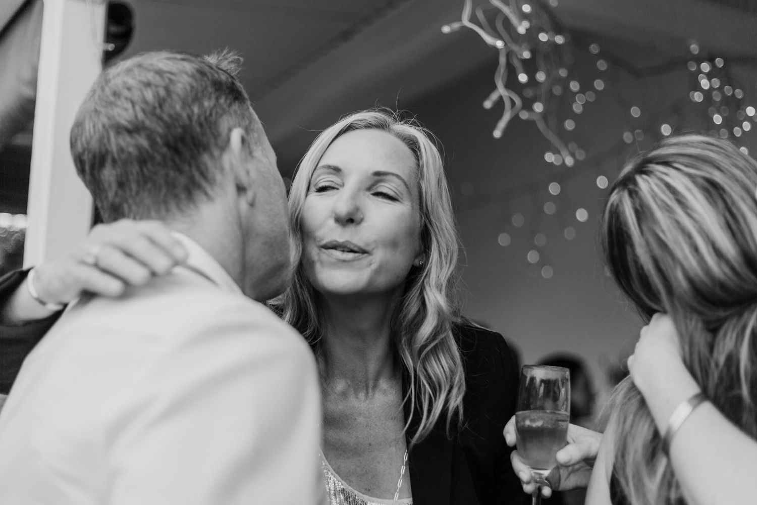 Woman smiling with closed eyes at a party while holding a glass of champagne in black and white.