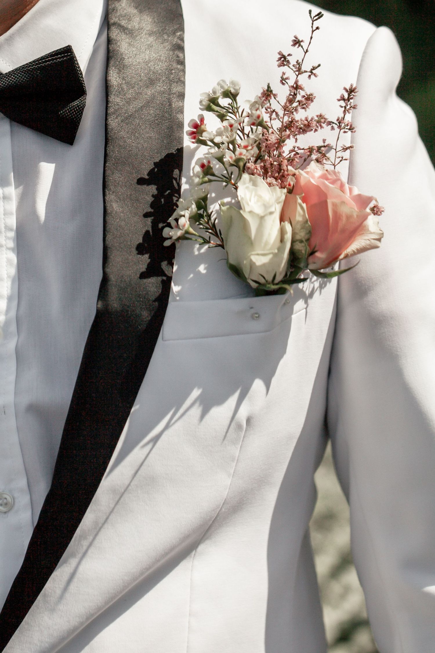 A white and black tuxedo lapel adorned with a delicate pink and white rose boutonniere.