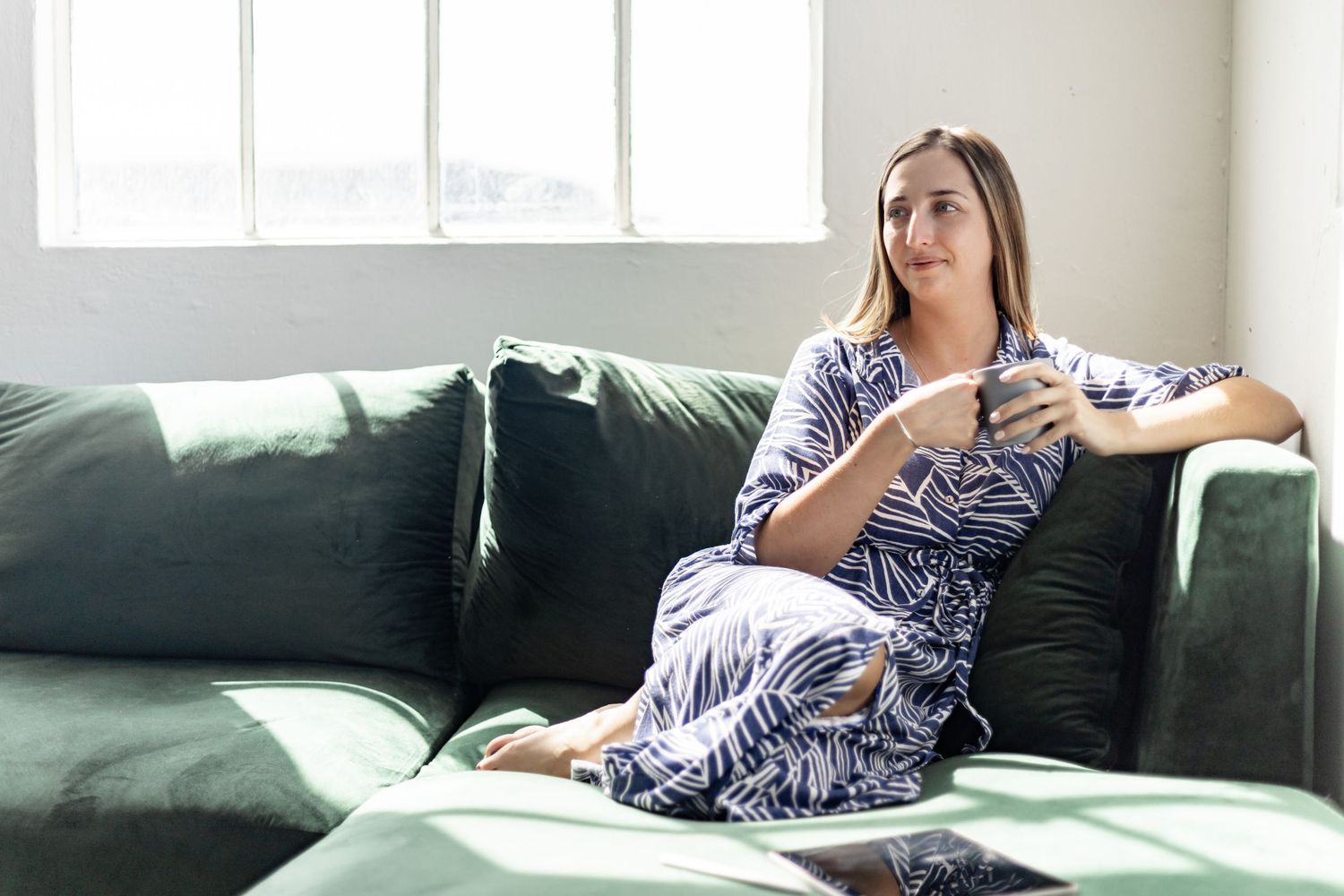 Person relaxing on a green couch in a bright room wearing blue and white striped shirt and jeans.