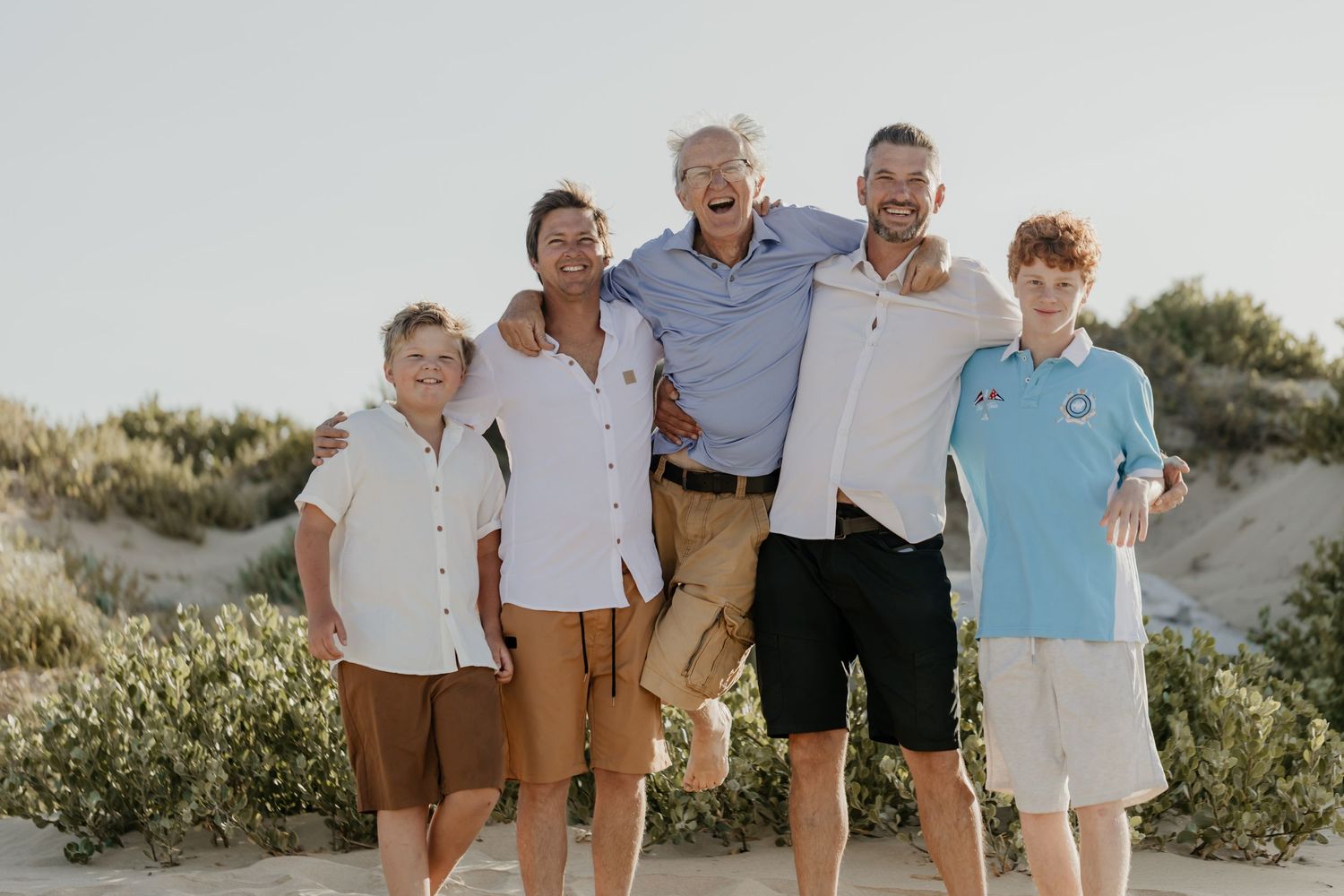 A joyful family group shares laughter while posing together on a sandy beach at sunset.
