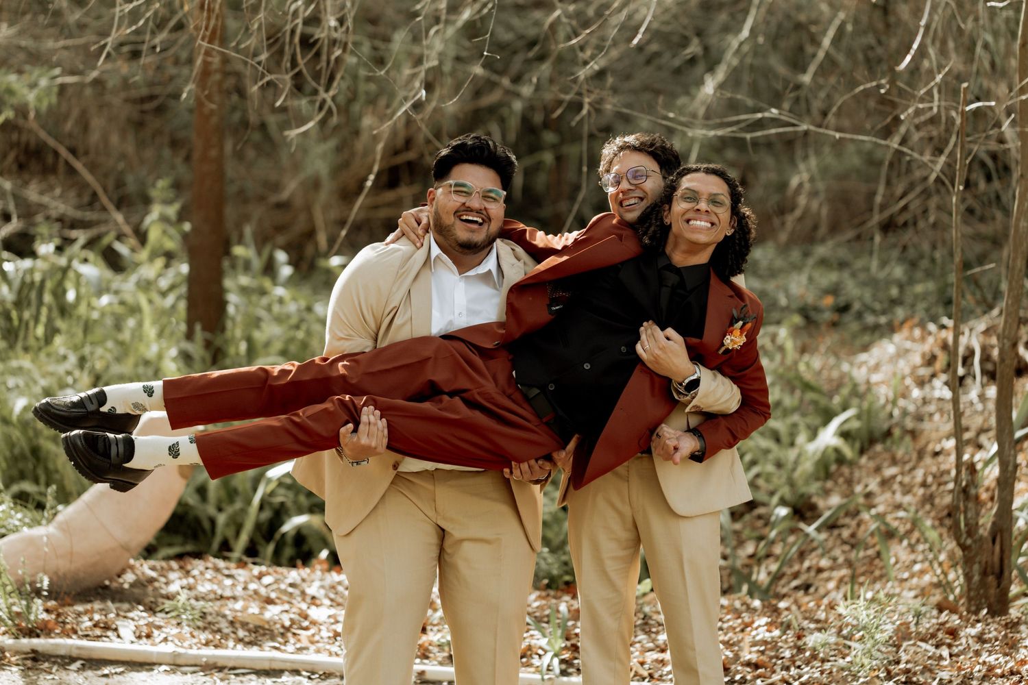 A playful group in burgundy sweaters and khaki pants pose for fun outdoor photos while frolicking on grass.