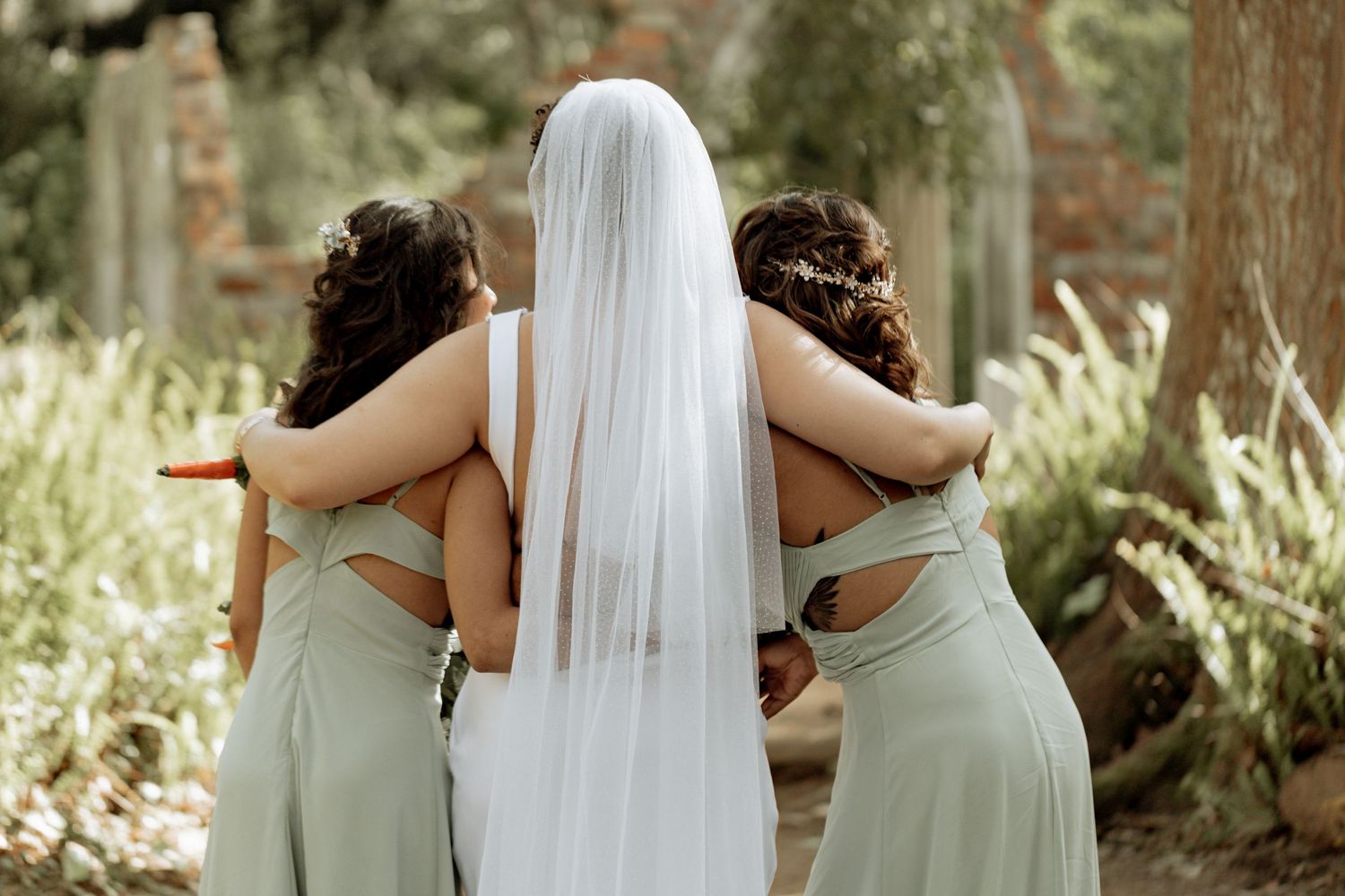 Wedding party lined up outdoors with bridesmaids in sage green dresses and bride in white gown with flowing veil.