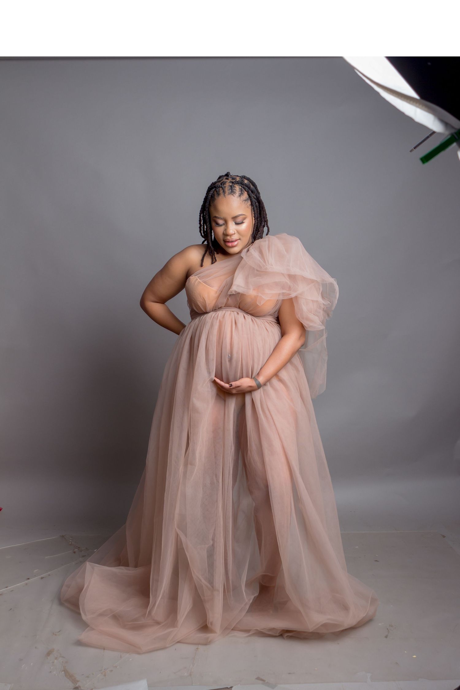 Studio portrait with ethereal pink tulle gown during maternity photoshoot against grey backdrop.