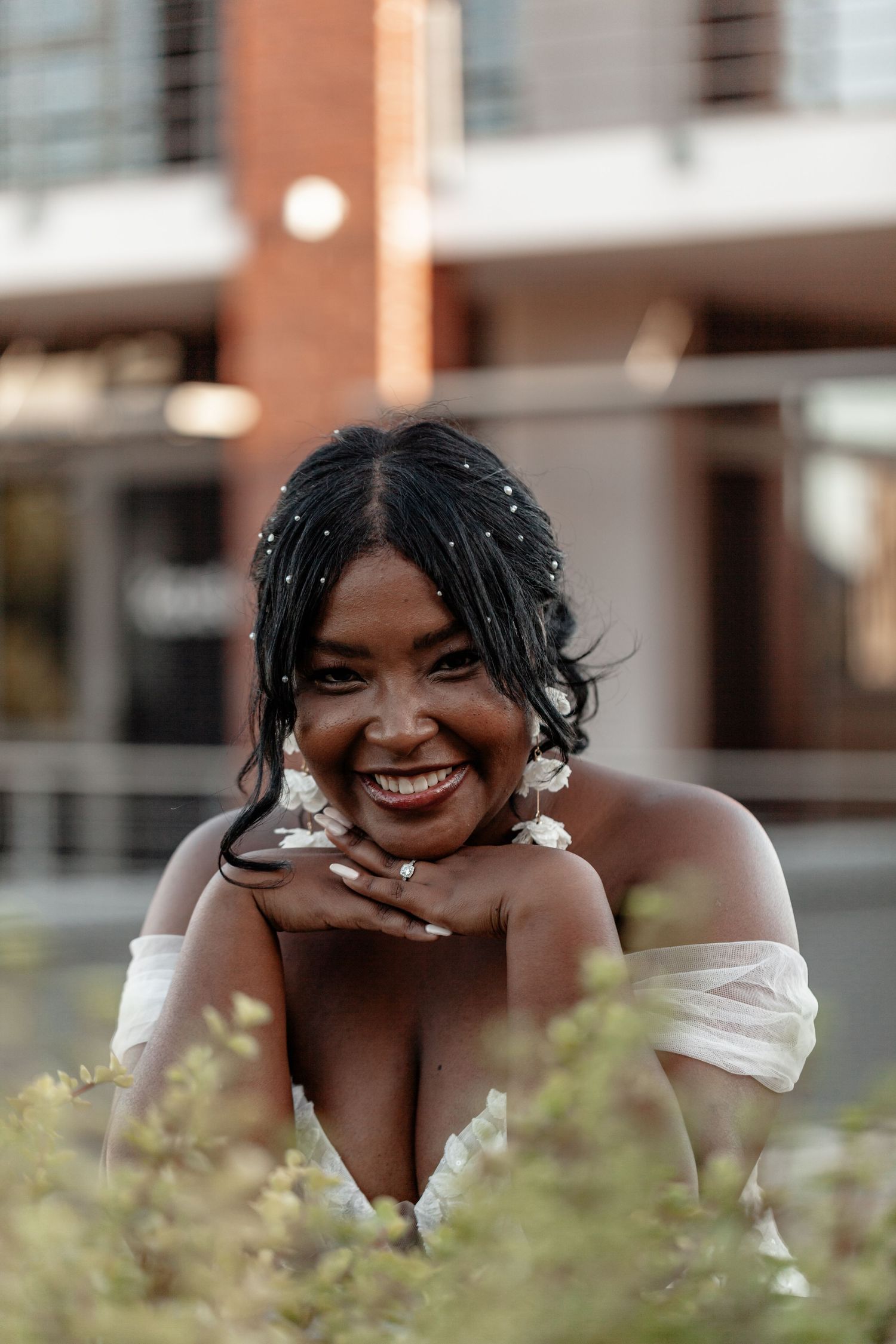 Joyful bride wearing off-shoulder wedding dress poses in an outdoor garden setting.