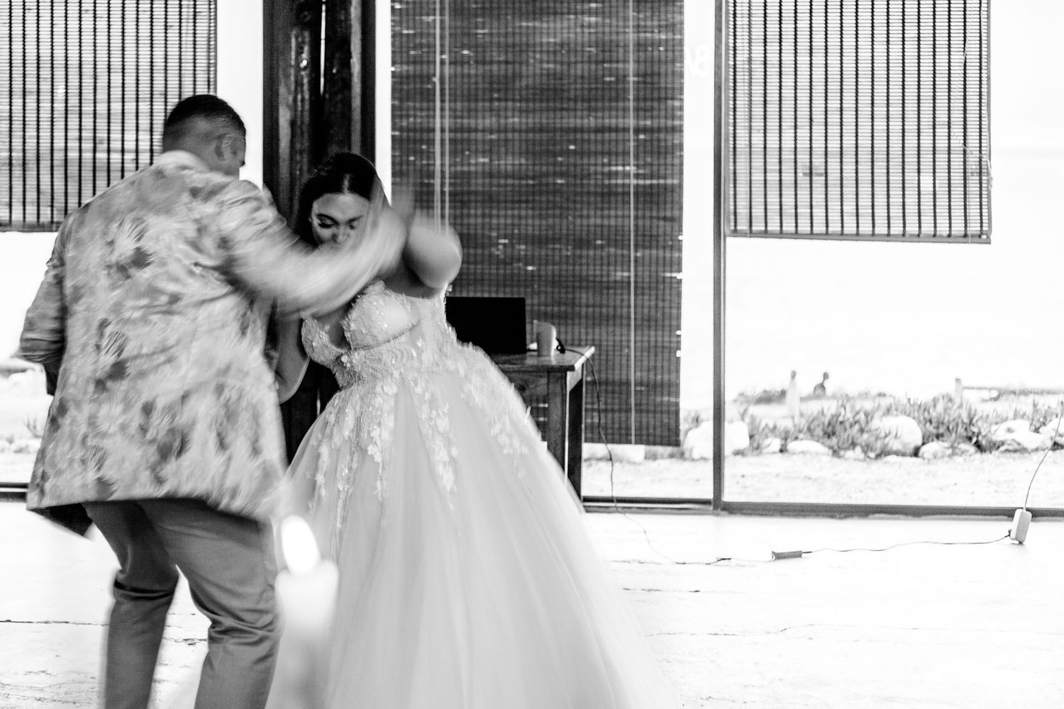 A tender black and white moment captured between a couple at a venue entrance with glass walls and vertical lines.