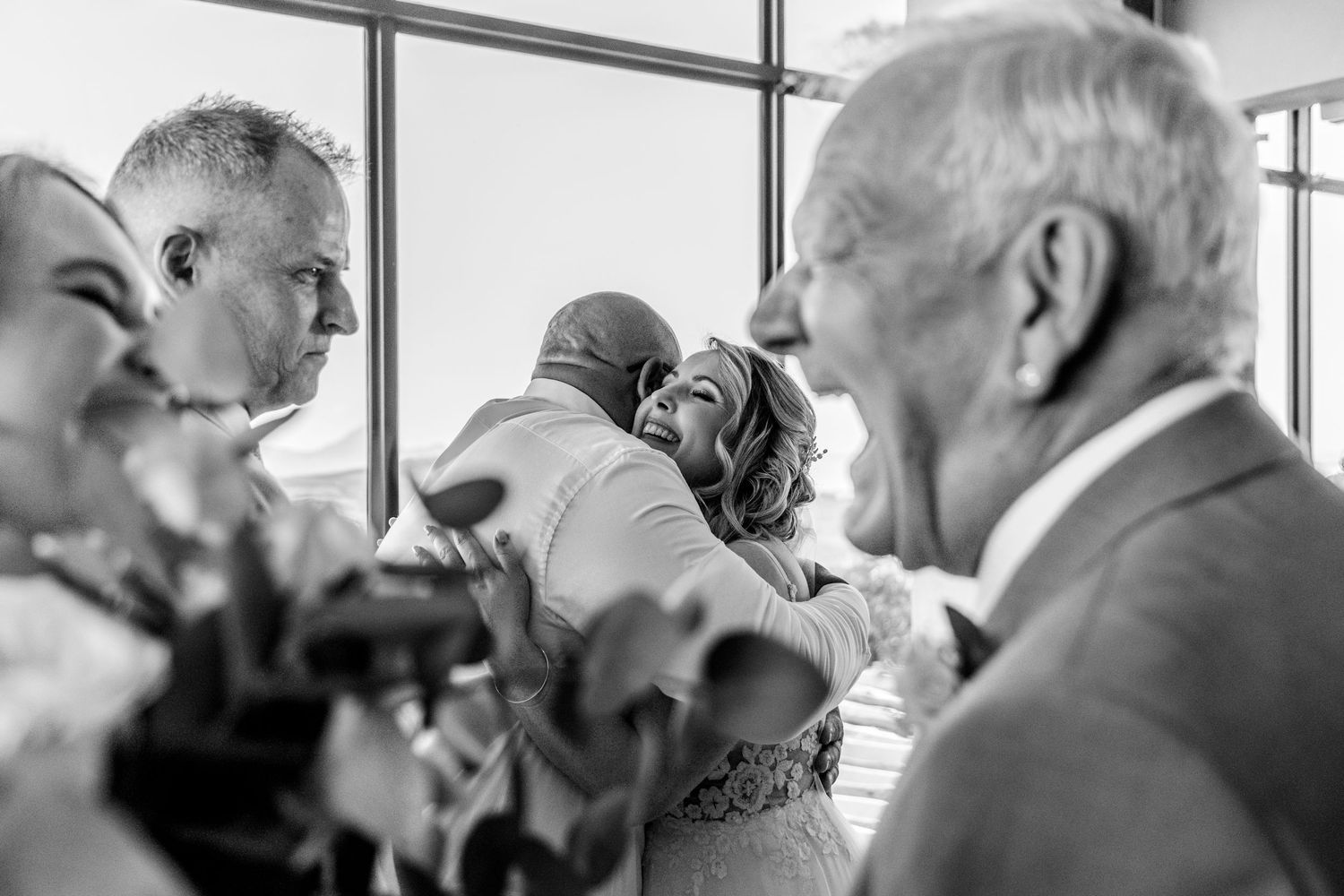 Black and white photo showing people gathered together at an event with a bright window in the background.