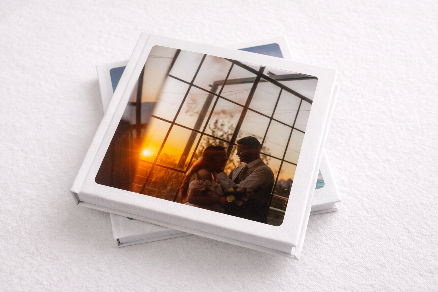 Stack of printed photographs scattered on white textured surface with warm sunset lighting in corner image.