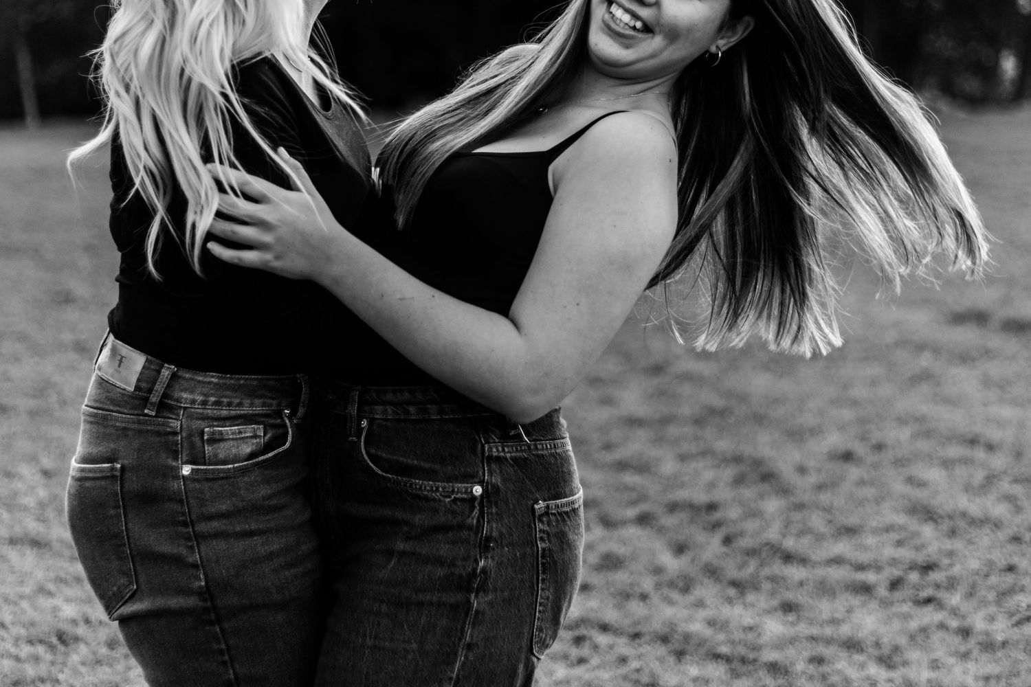 A couple in denim jeans embracing and laughing together outdoors in black and white photography.