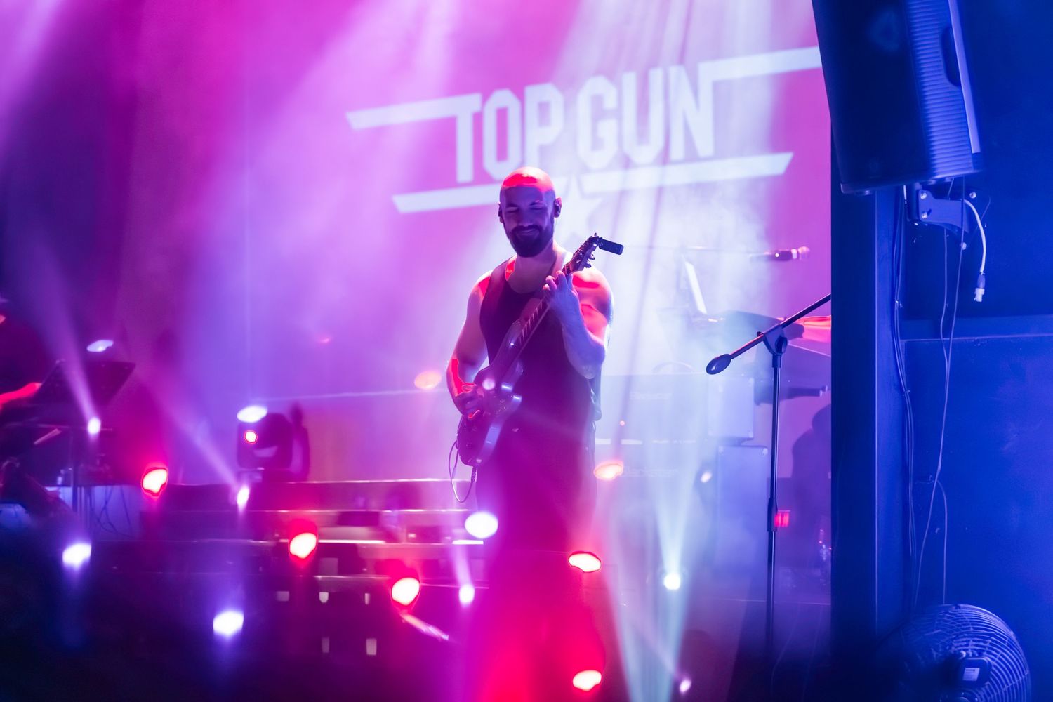 Musician performing on stage at a Top Gun themed concert with vibrant purple and red stage lighting.