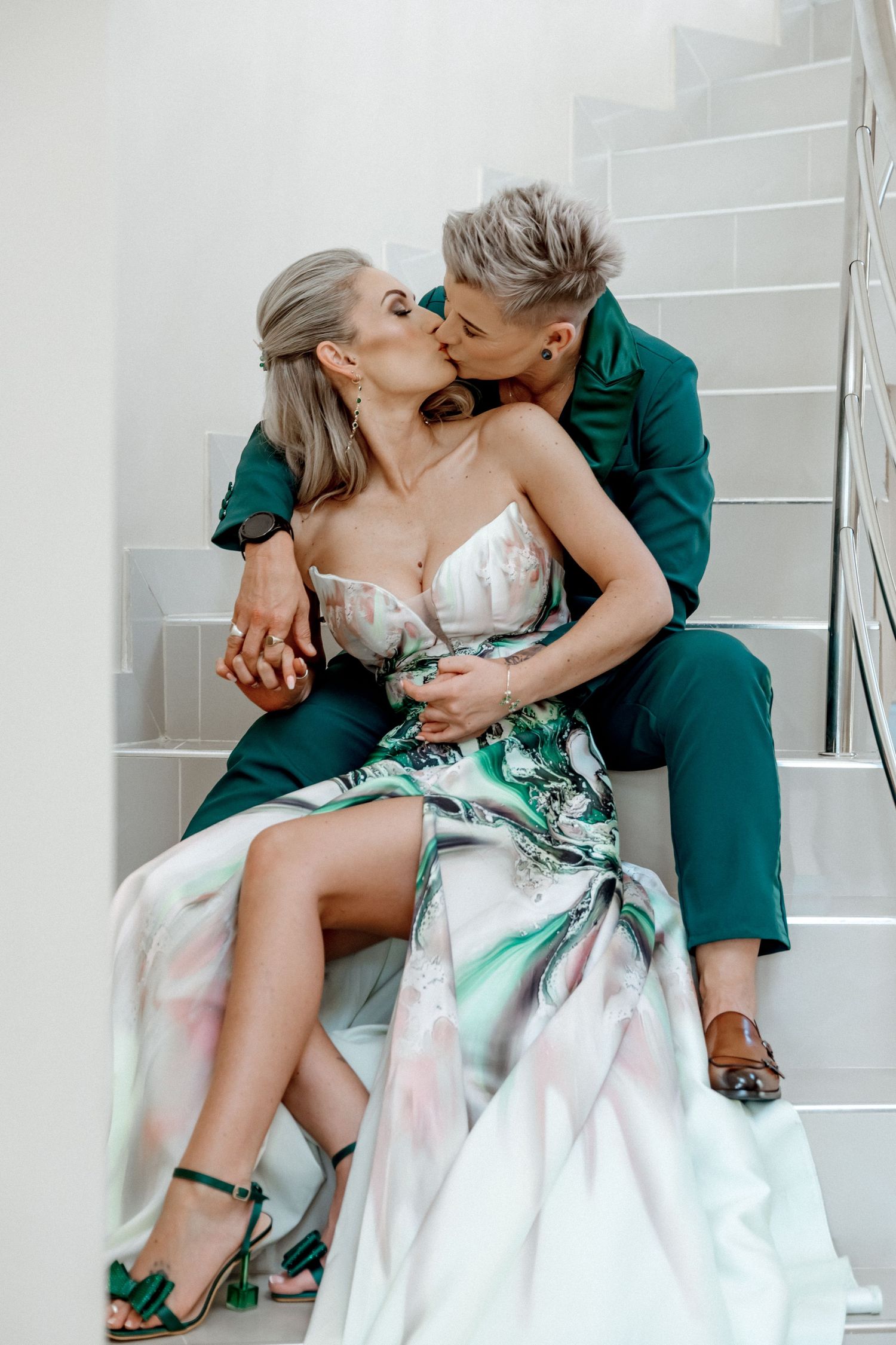 A romantic couple in wedding attire sharing an intimate moment on white stairs, with emerald green accents.