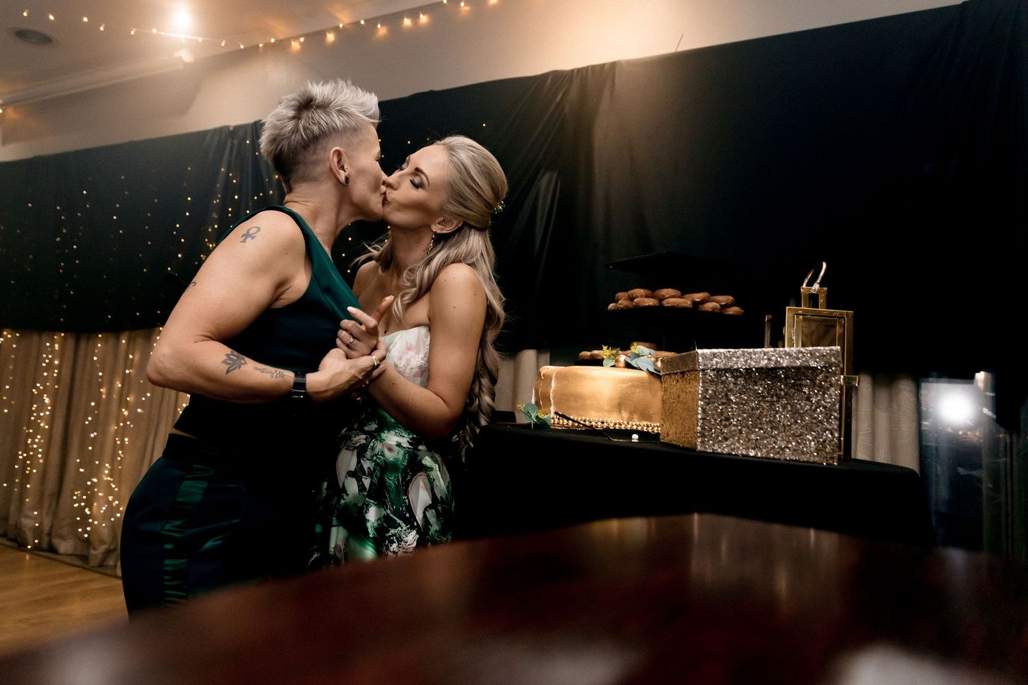 Two people share a romantic moment on a dance floor with twinkling string lights and decorations in the background.