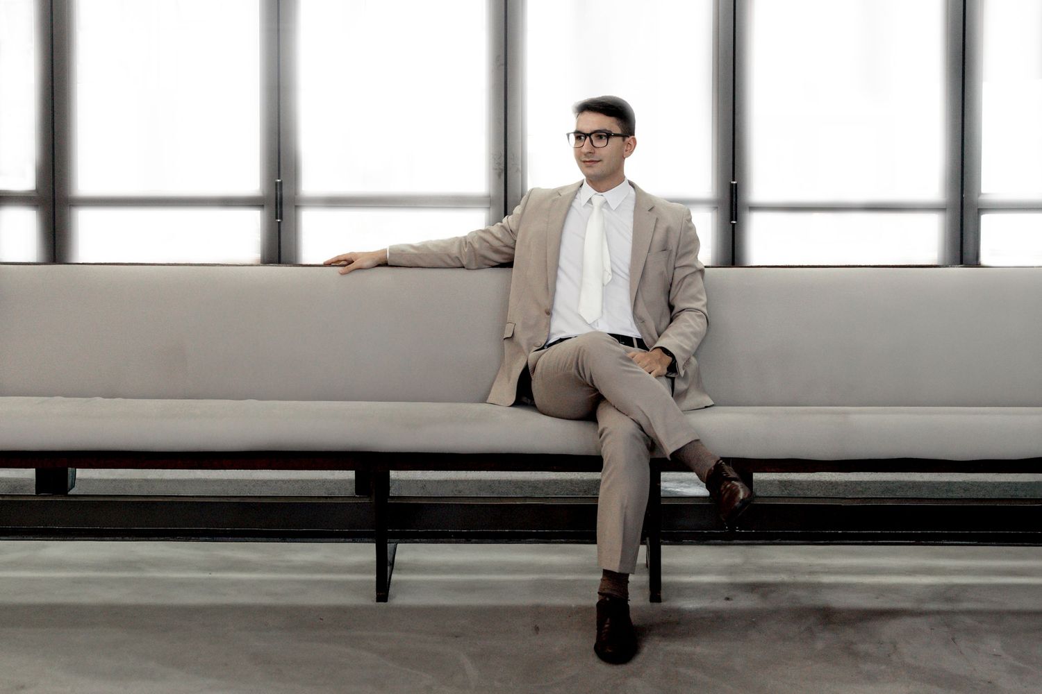 Professional in a beige suit sits alone on a modern bench in a minimalist interior space.