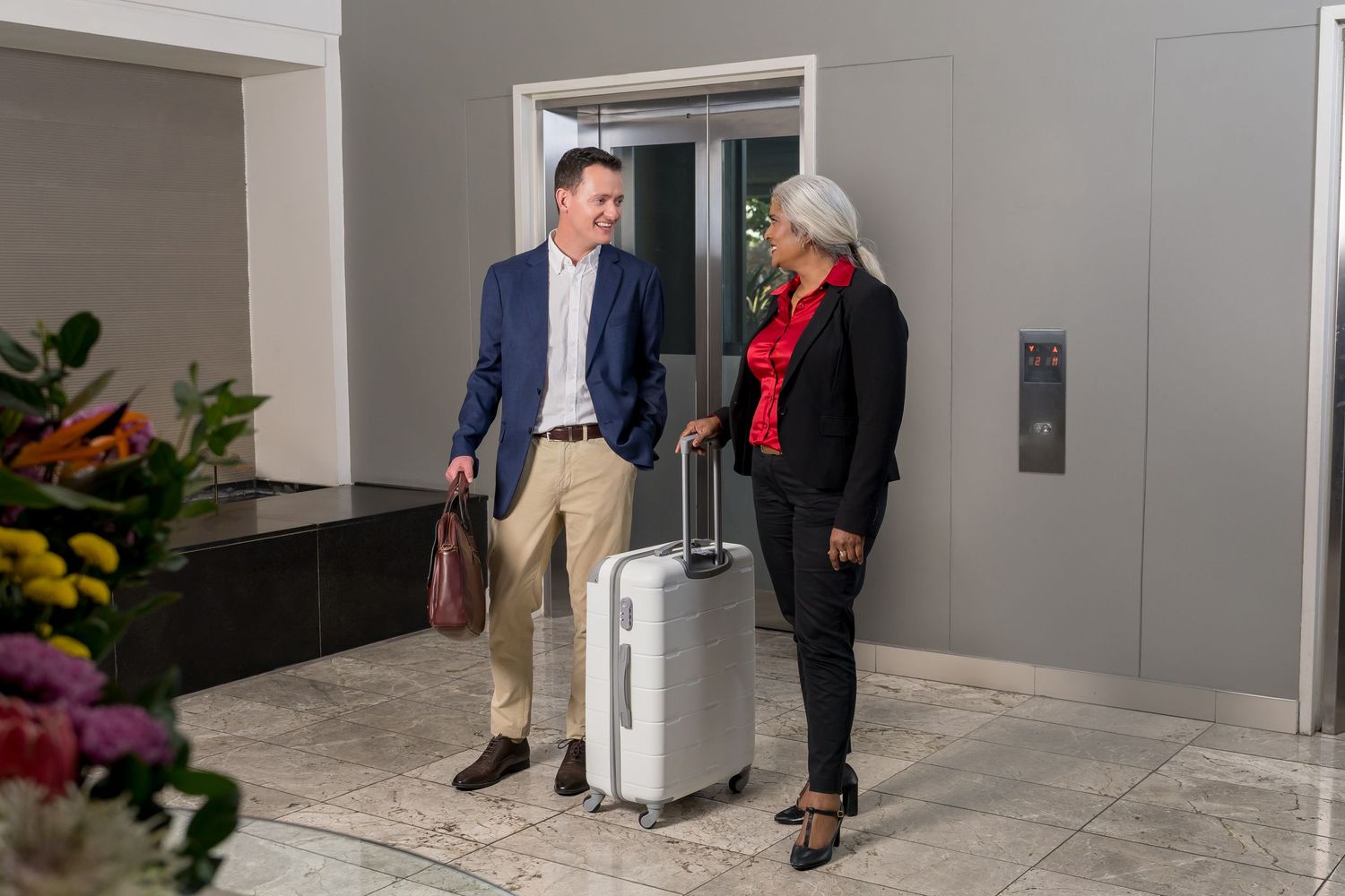 Professional meeting scene in modern office hallway with luggage and people in business attire.