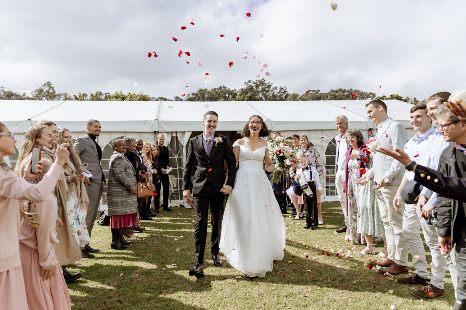 Wedding guests release pink heart-shaped balloons into the sky during an outdoor waterfront celebration.