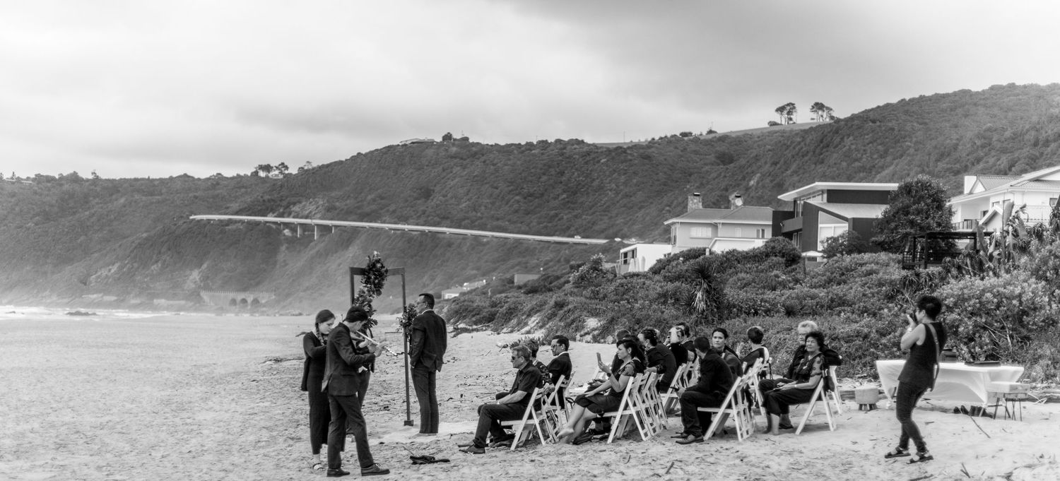Beachgoers relax in chairs on a foggy coastal California shoreline while others stand near cliffside buildings in 1930s.