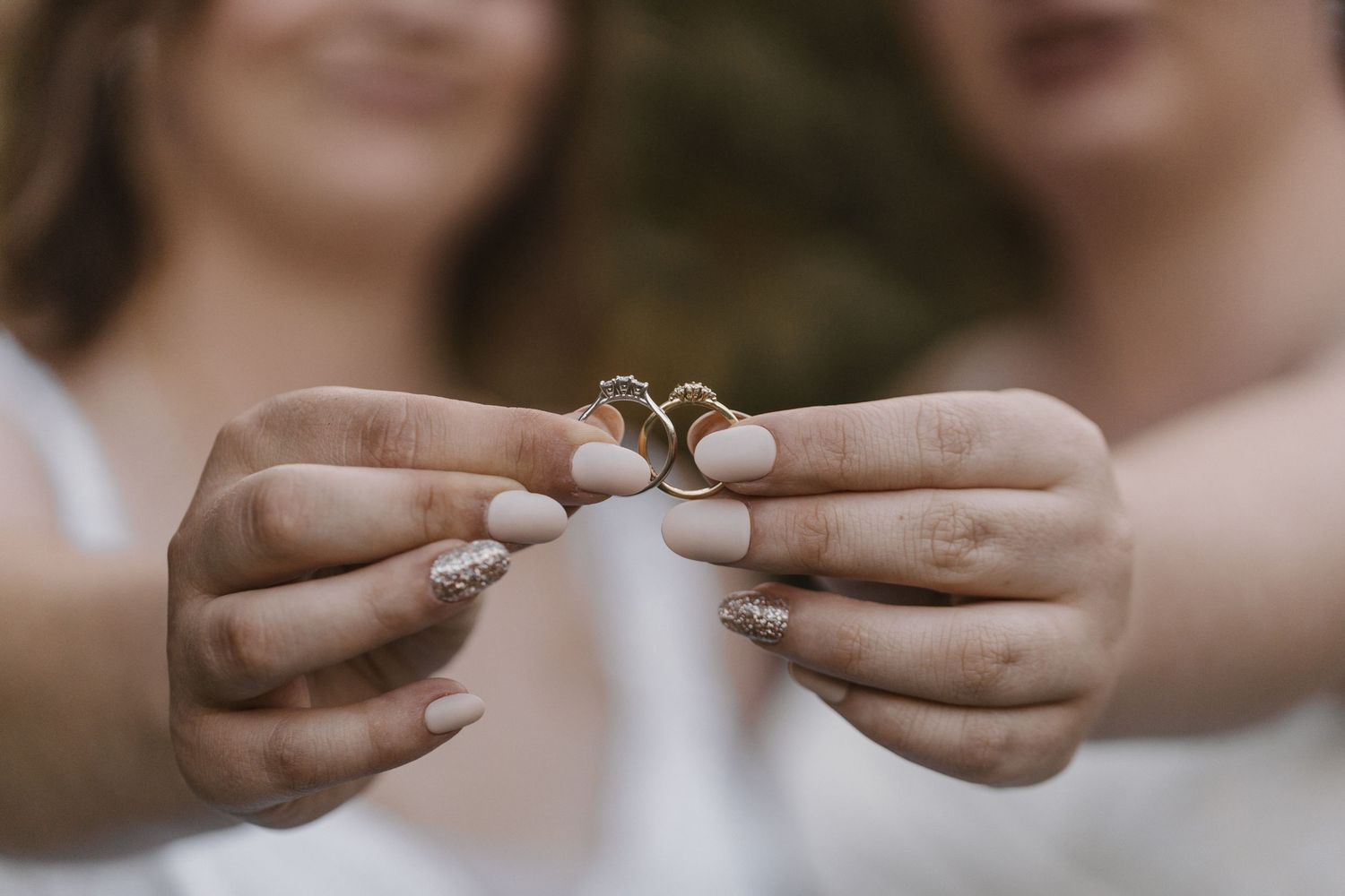 Two hands holding wedding rings together in a close-up shot with soft blurred background.