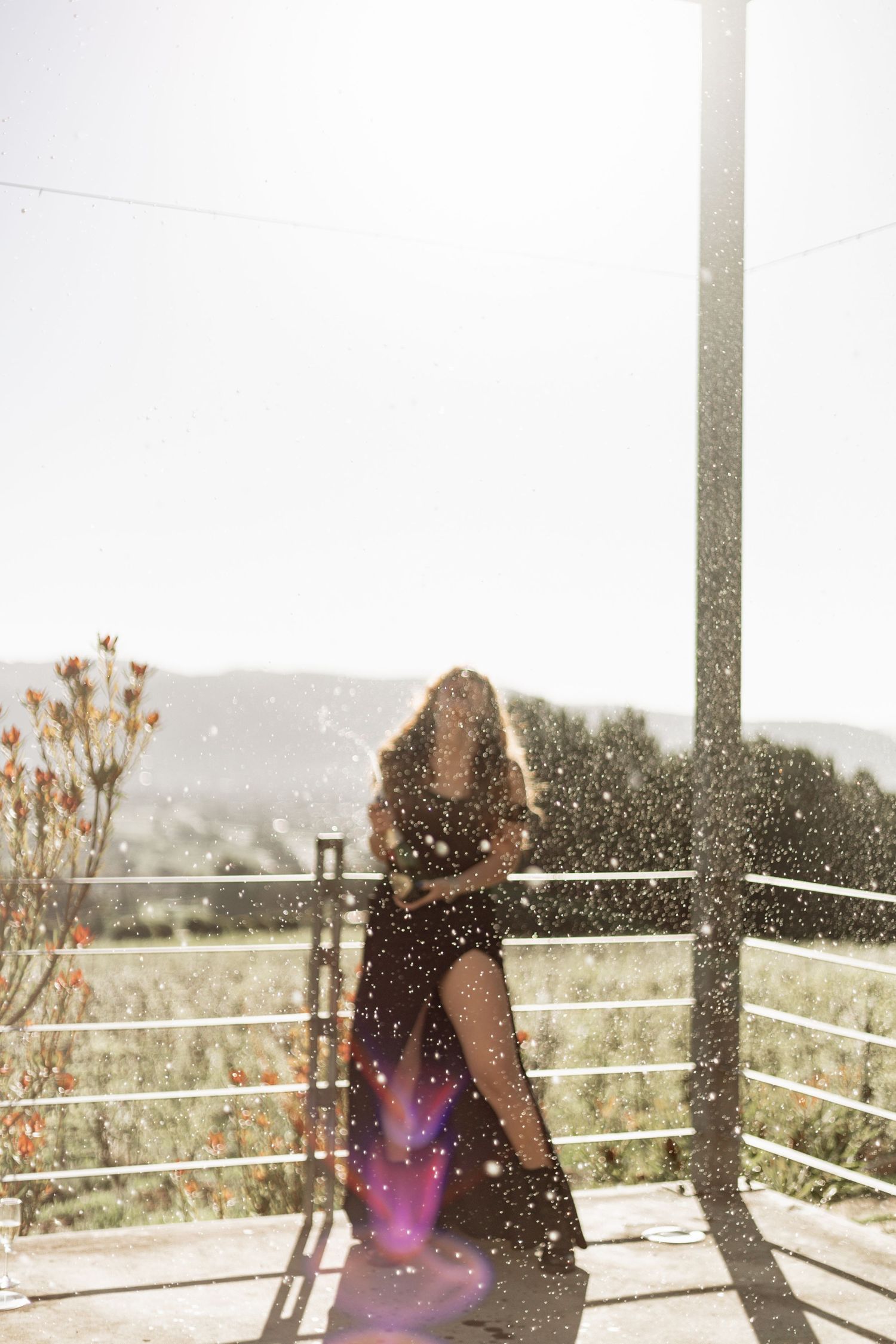 Person sitting alone on a wooden deck railing overlooking mountains with a dreamy sun glare effect.