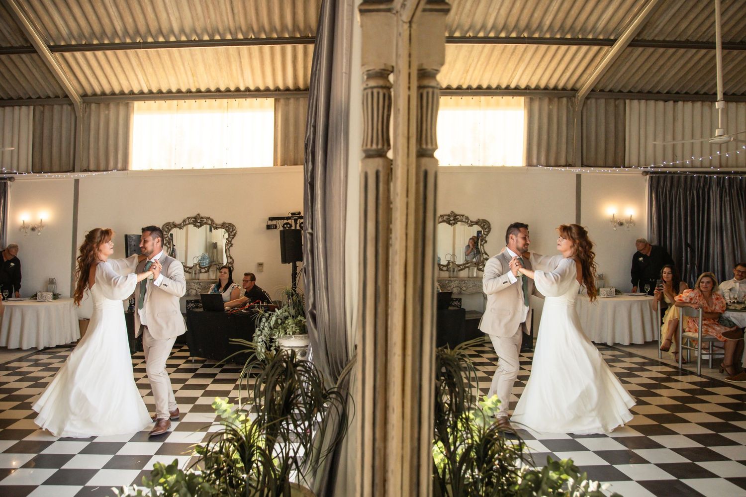 Bride and groom sharing first dance reflected in mirror on checkered floor at wedding.
