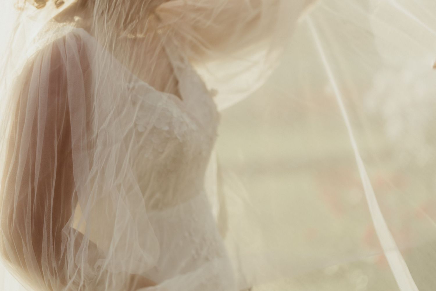 Delicate white wedding dresses hang in a row against a soft beige background creating an ethereal display.