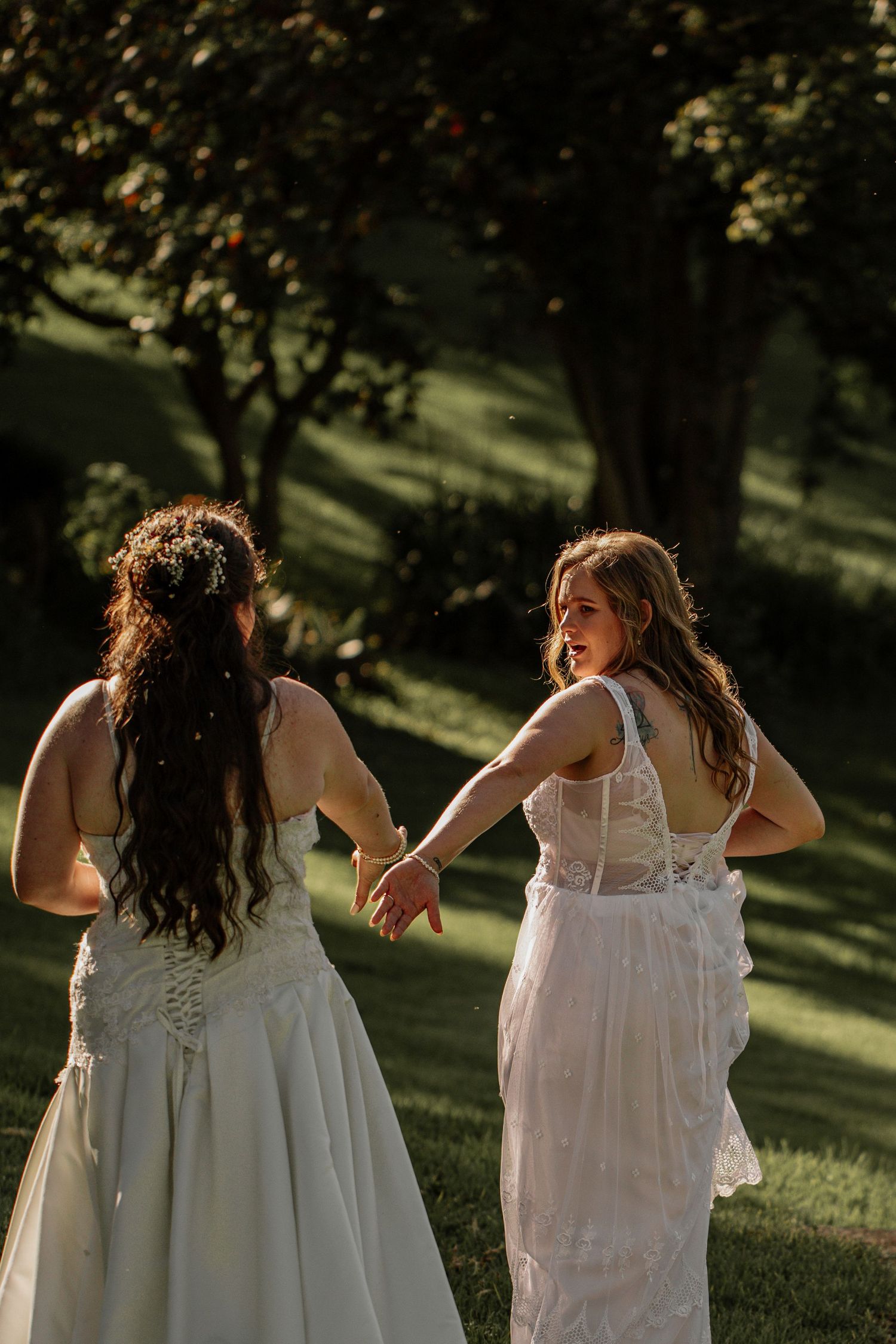 Women in white dresses walk together on a sunny grassy lawn during a summer photoshoot.