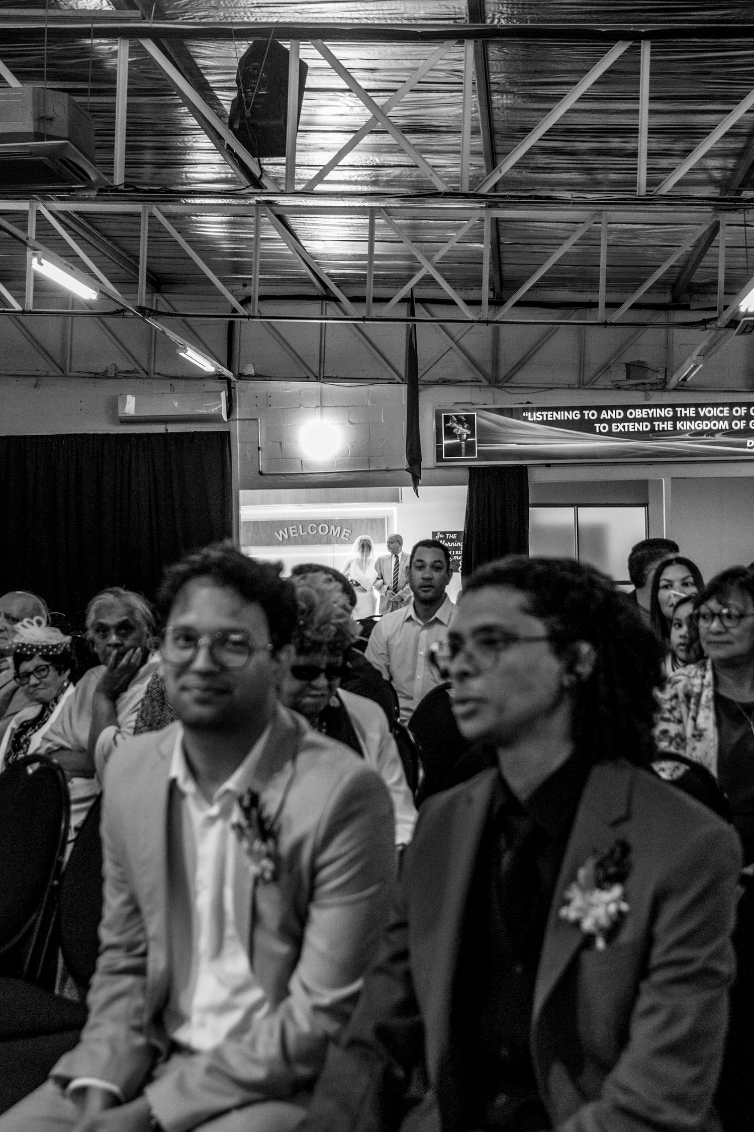 Black and white photo showing audience members seated at an event in a large industrial indoor space.