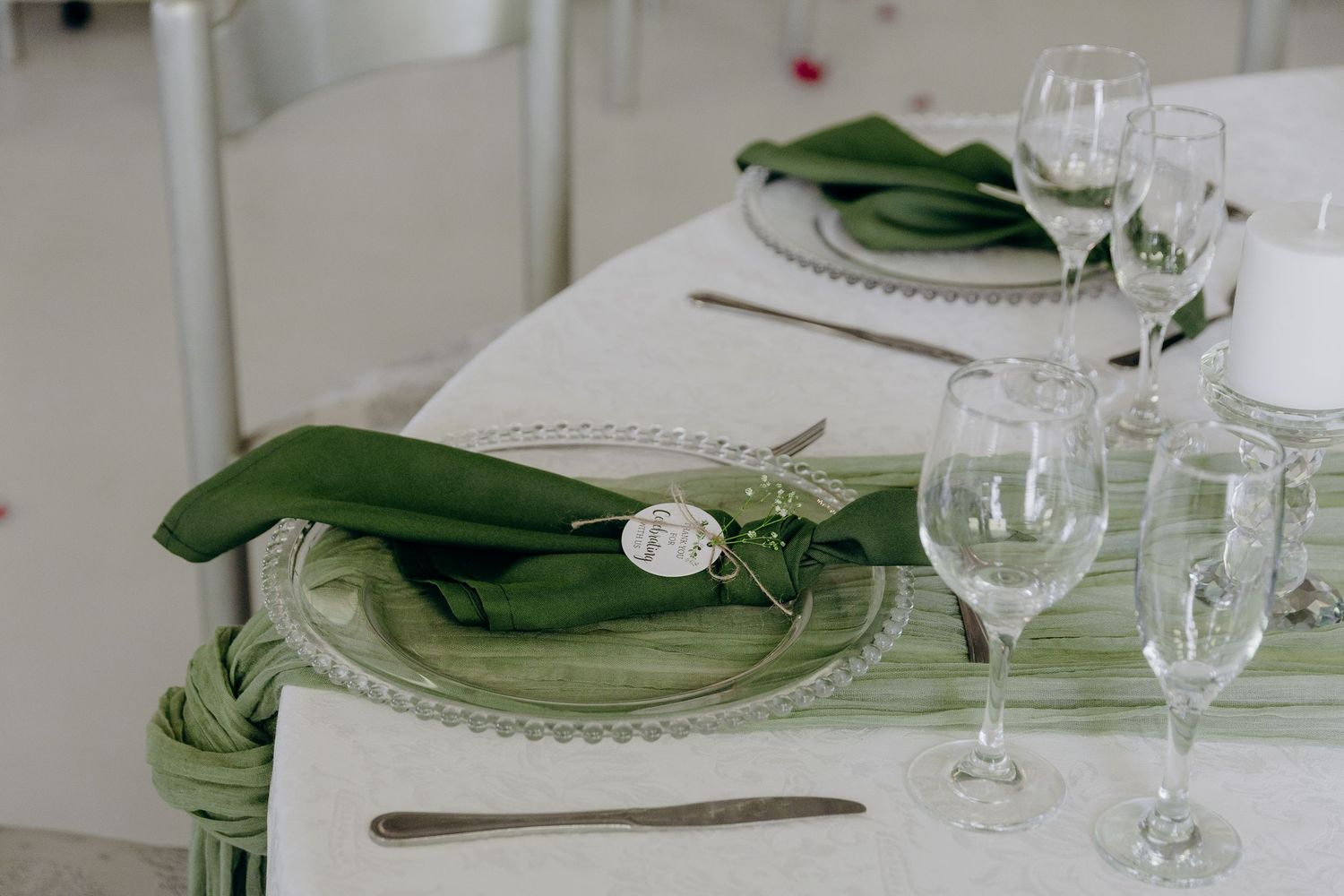 Elegant table setting with green napkins, wine glasses, and white plates arranged in a formal dining setup.
