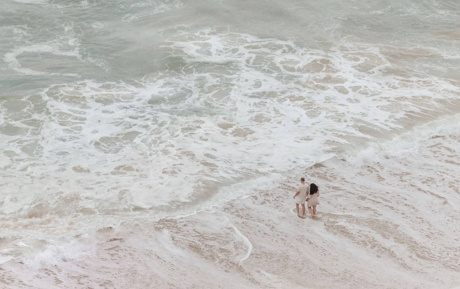 Aerial view of waves crashing onto a sandy beach with white foam patterns creating natural textures in the water.