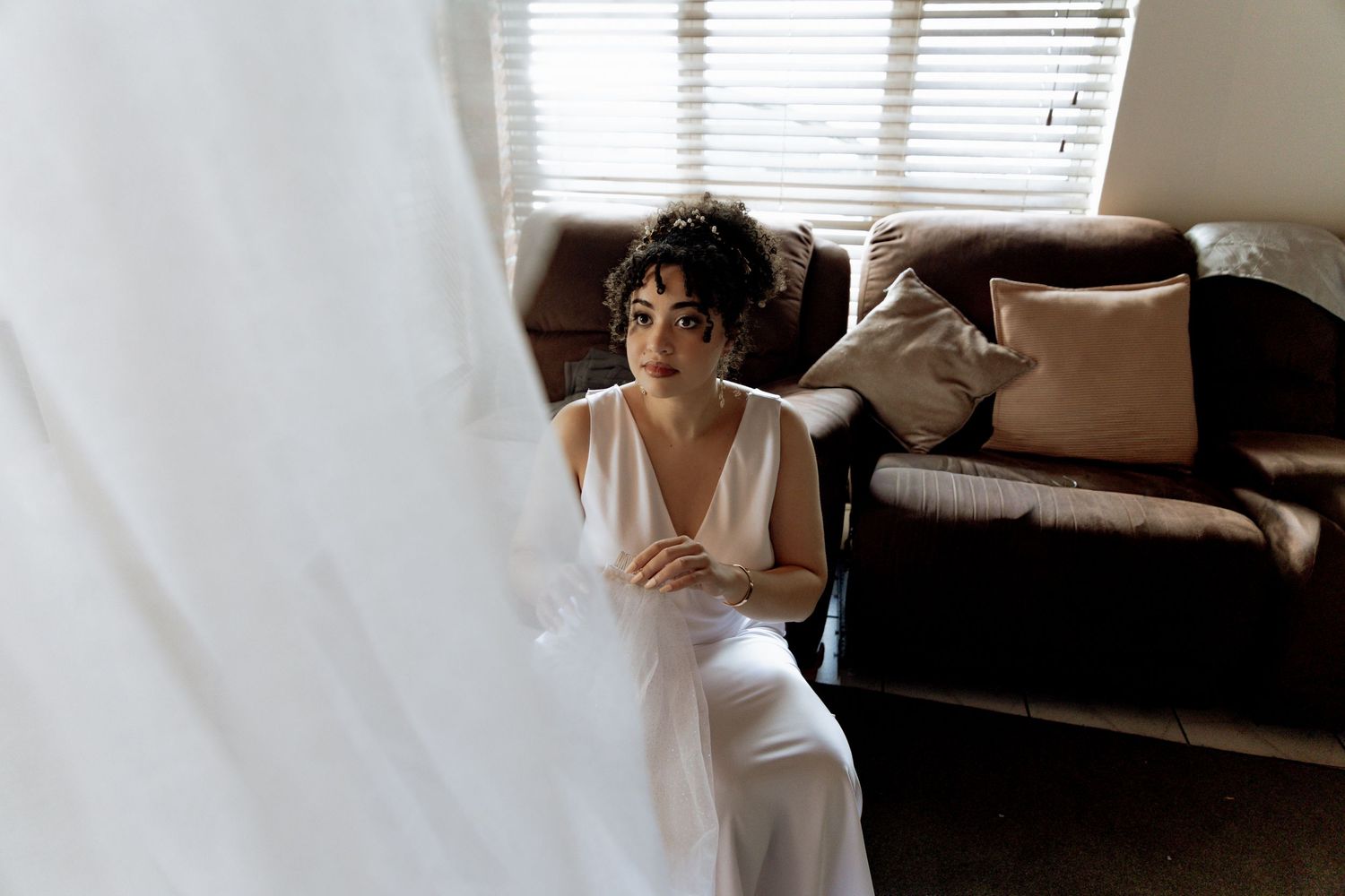 A bridal gown hangs from a white doorway, showcasing delicate lace details and flowing fabric in natural light.