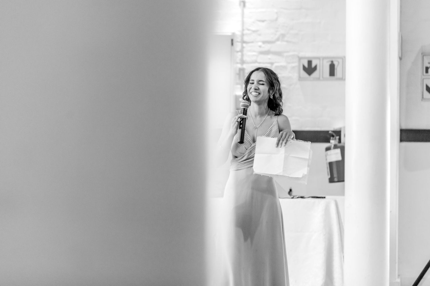 A person in a wedding dress speaks into a microphone during a black and white reception moment.
