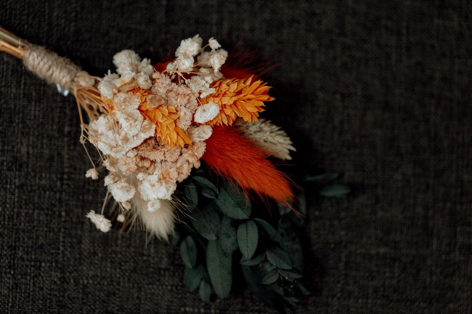 Two white fluffy kitten dolls with orange floral arrangement and dark green foliage on textured black backdrop.