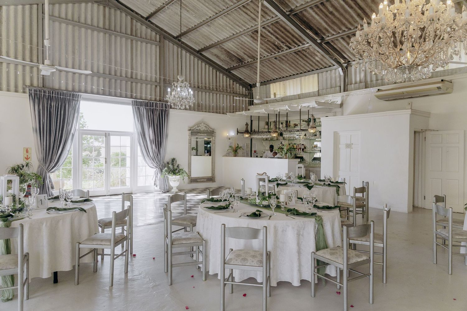 Elegant white wedding venue interior with crystal chandeliers, draped curtains, and modern industrial ceiling details.
